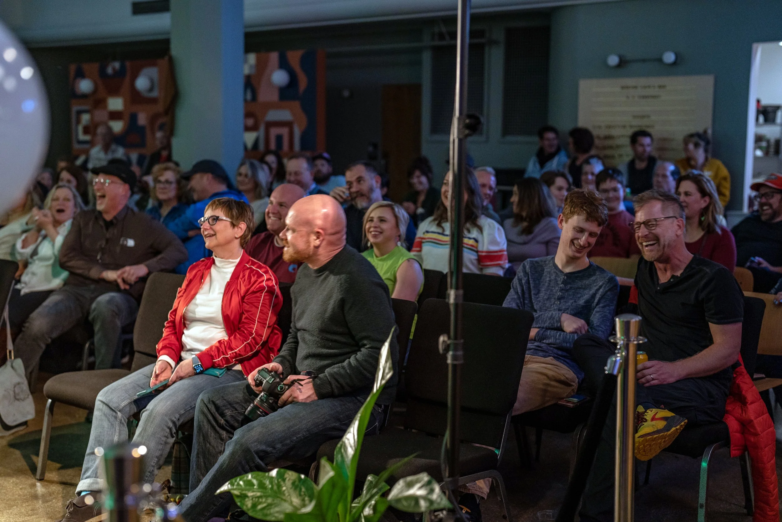 A group of people sitting and laughing at an indoor event or comedy show.