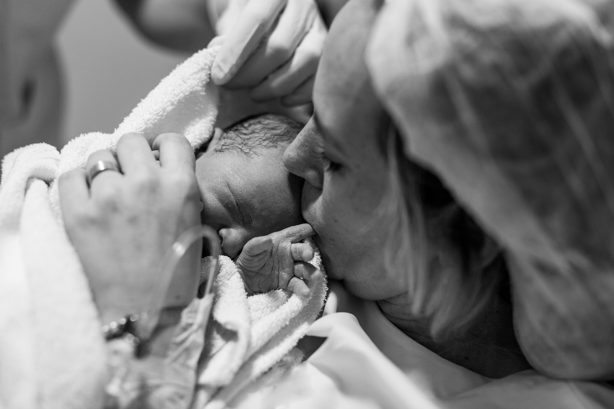 Black and white photo of a newborn baby wrapped in a blanket being kissed by a parent.