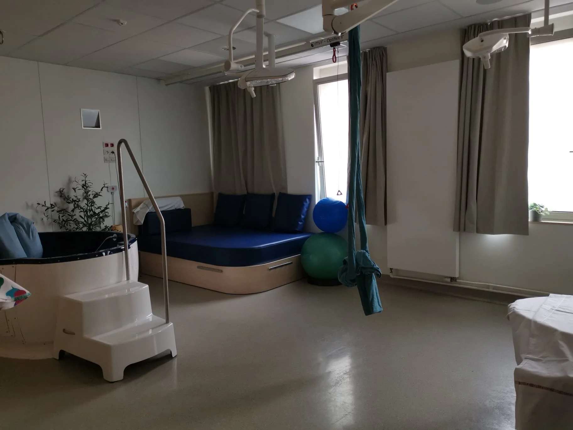 Hospital room with a birthing pool, bed, gym balls, and medical equipment.