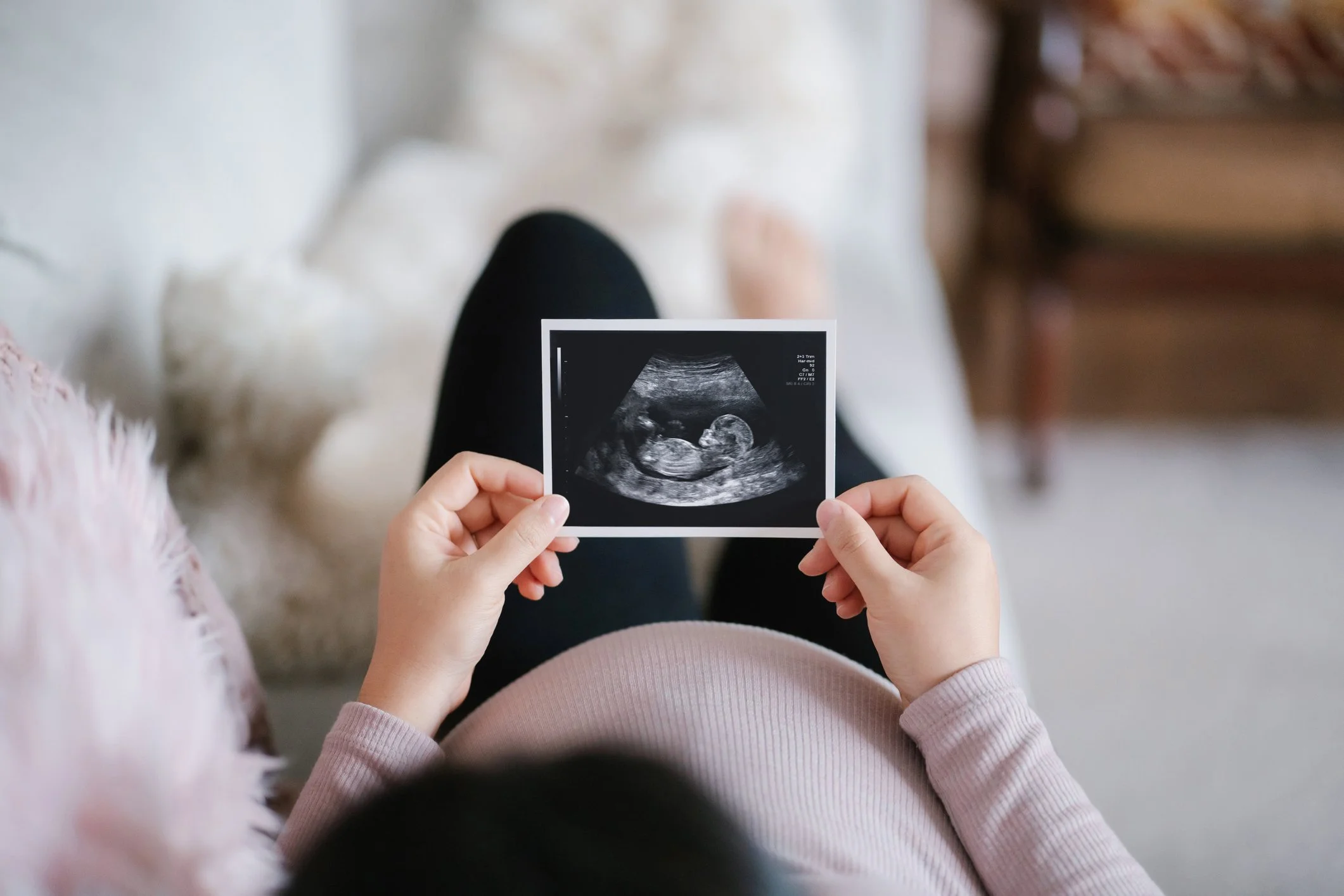 Pregnant woman holding a sonogram image, sitting on a couch.