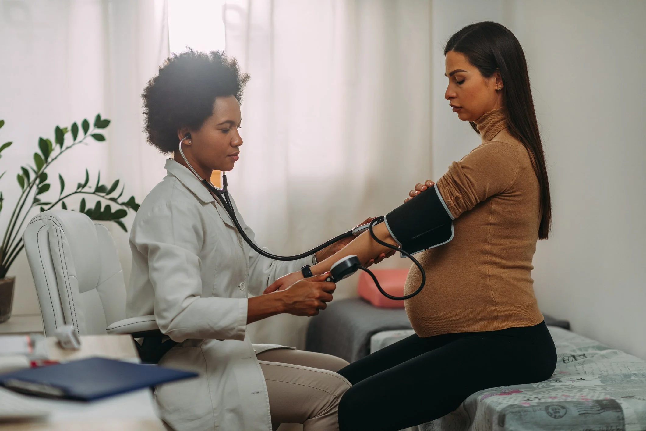 A healthcare professional checks a pregnant woman's blood pressure using a sphygmomanometer in a clinic.