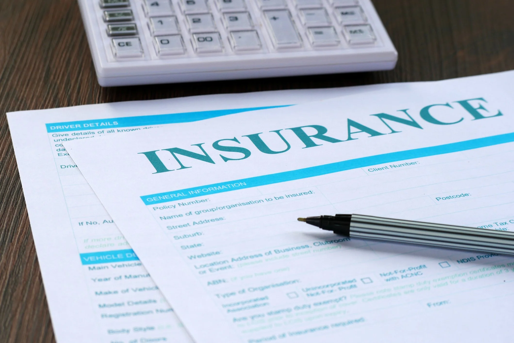 Insurance application form with a black and white striped pen, placed on a wooden surface, and a calculator in the background.