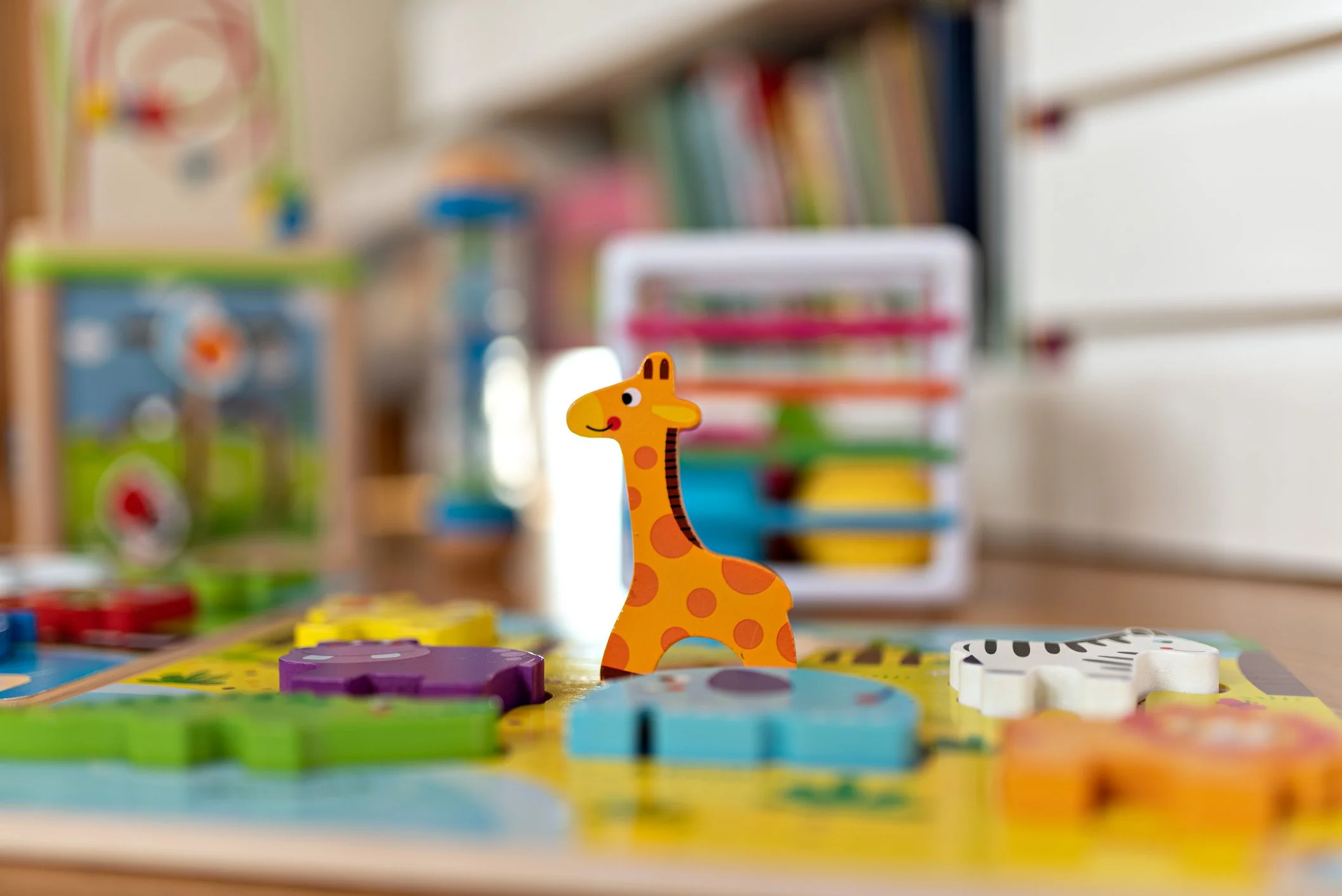Colorful children's board game with a giraffe game piece in the foreground, blurred game pieces and shelves in the background.