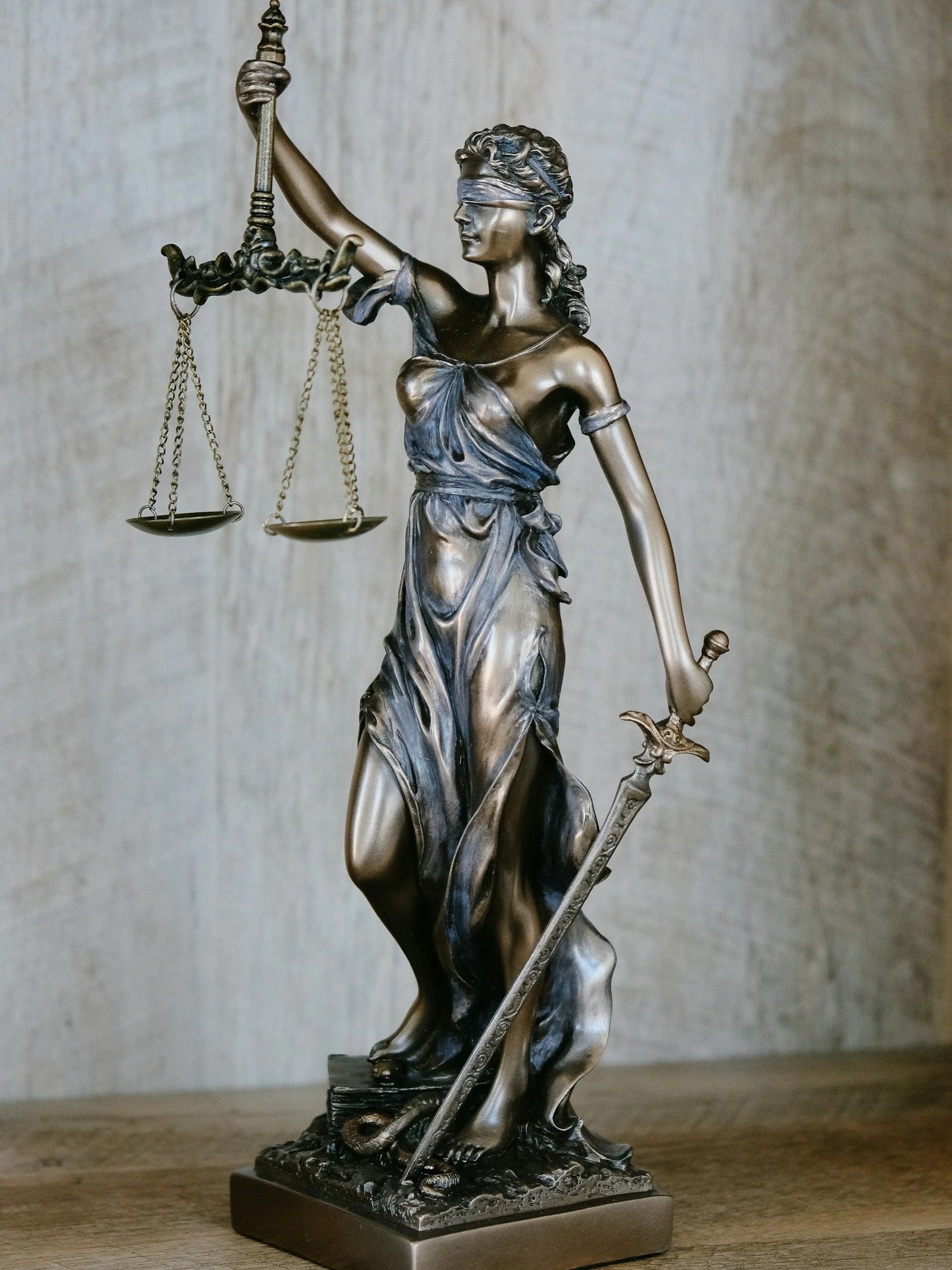 Bronze statue of Lady Justice holding a sword in her right hand and a set of scales in her left, with her eyes blindfolded.