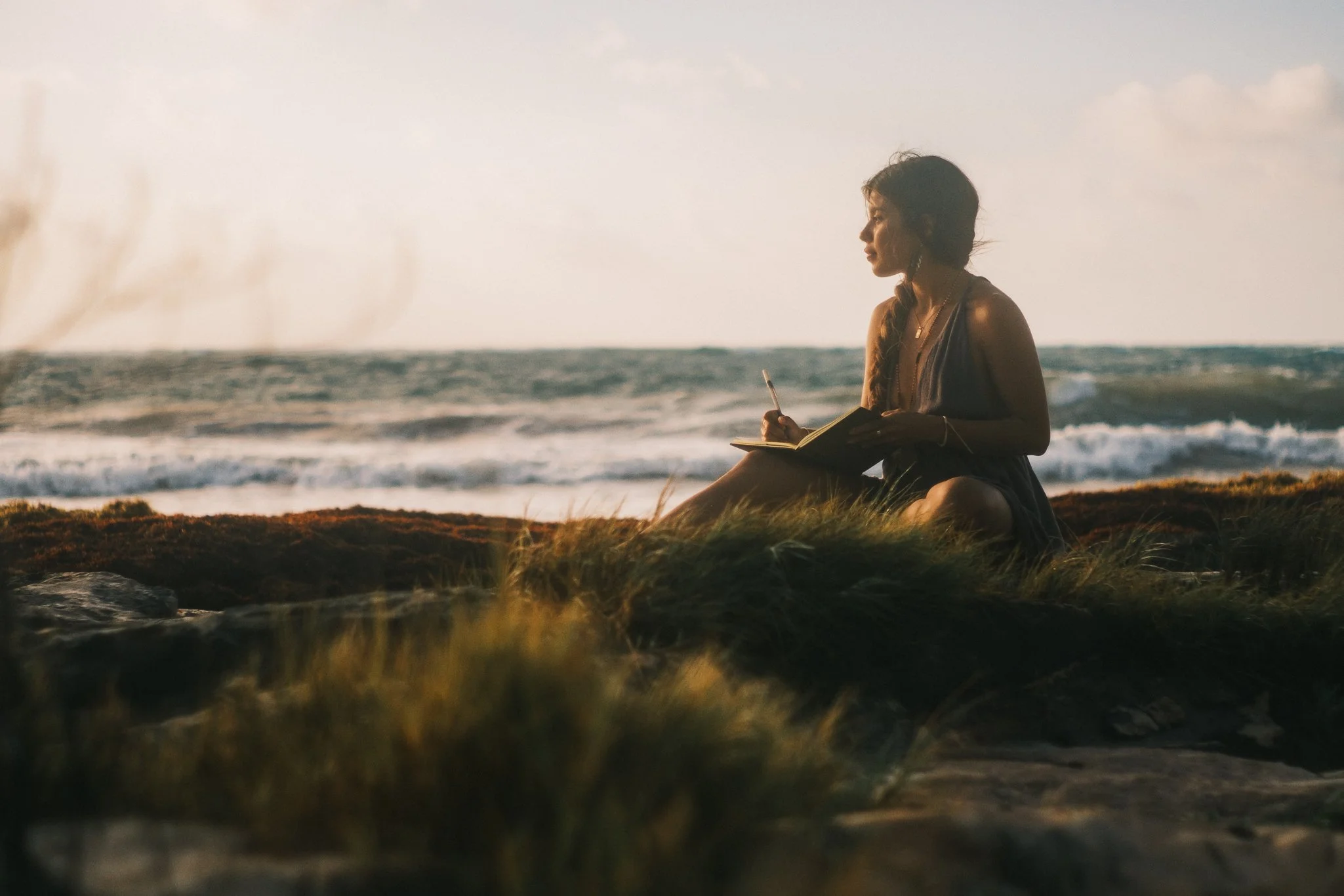 A woman sitting on the beach at sunset, writing in a journal.