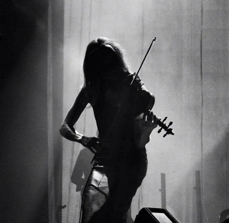 Silhouette of a woman playing the violin on stage with a spotlight behind her.