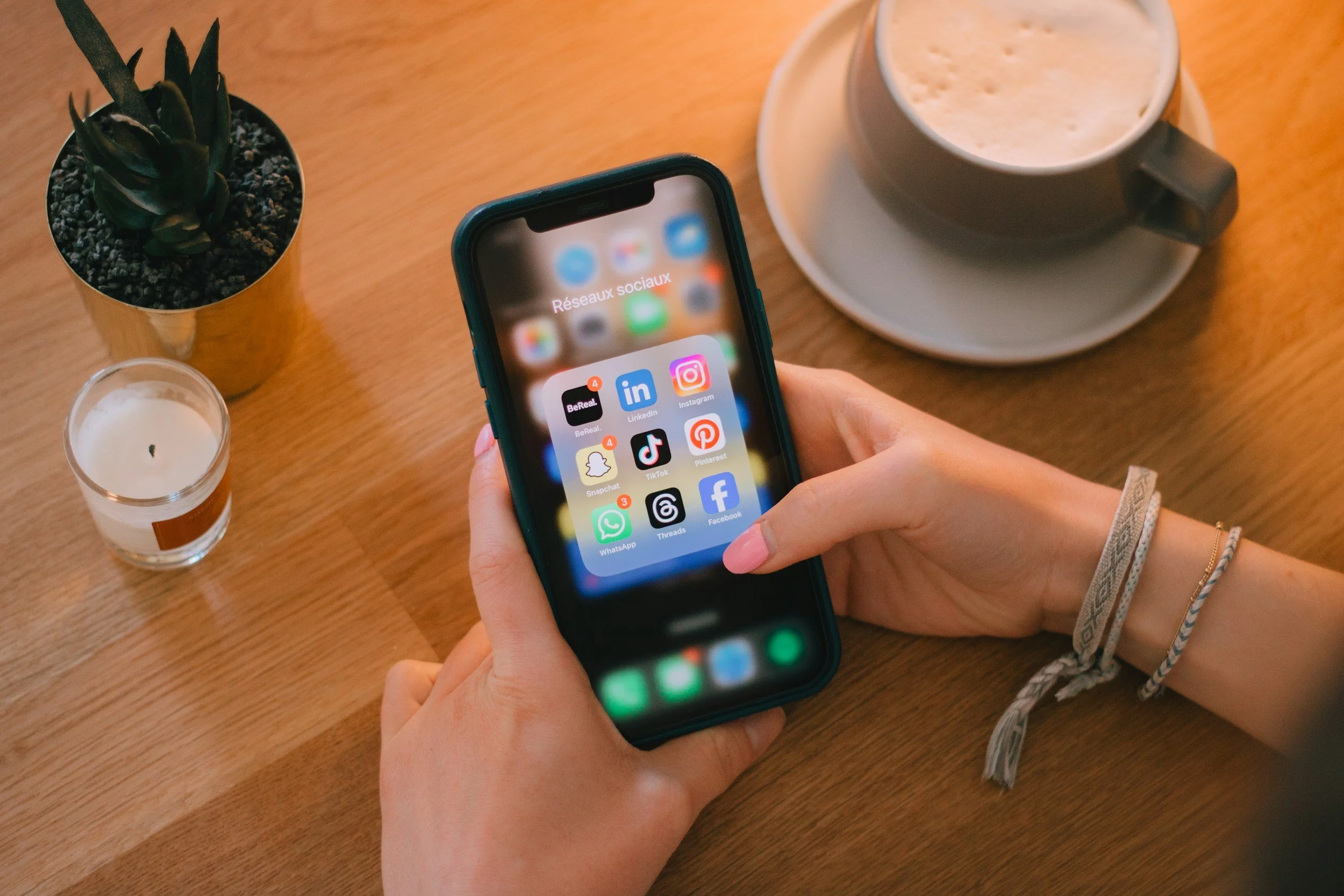 Closeup of a person seated at a table holding a phone displaying social media icons.