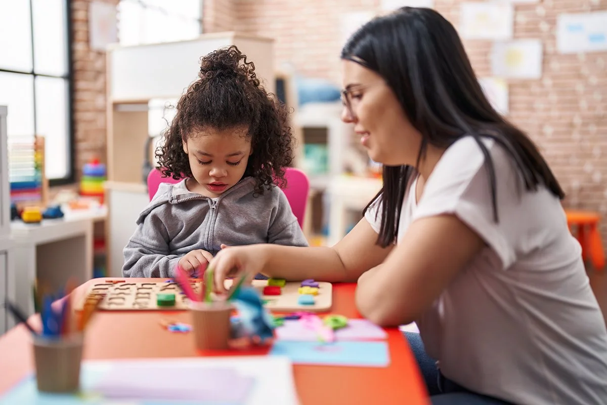 Teacher and young child playing a game at a table