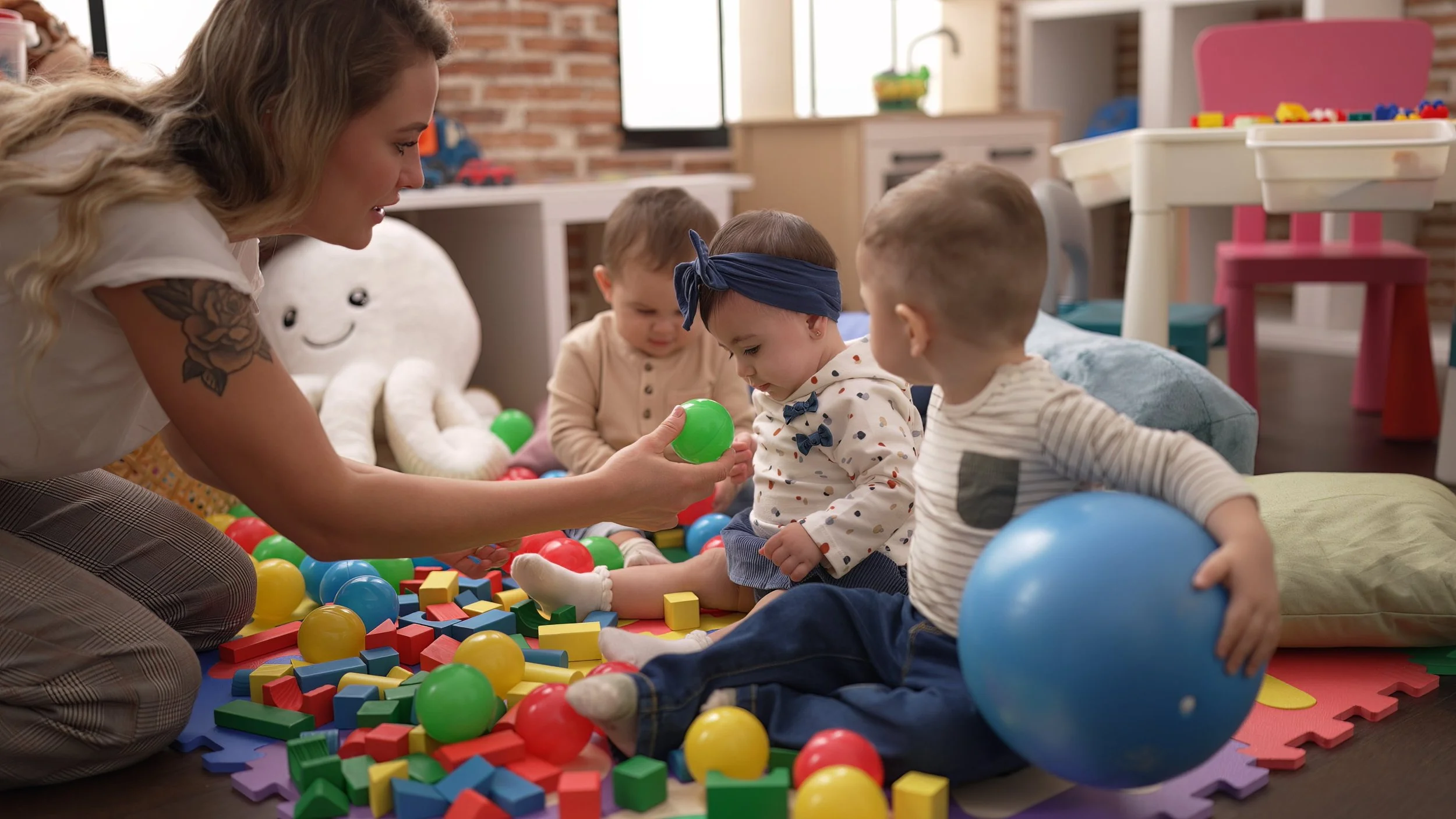 Female preschool teacher and toddlers playing with blocks