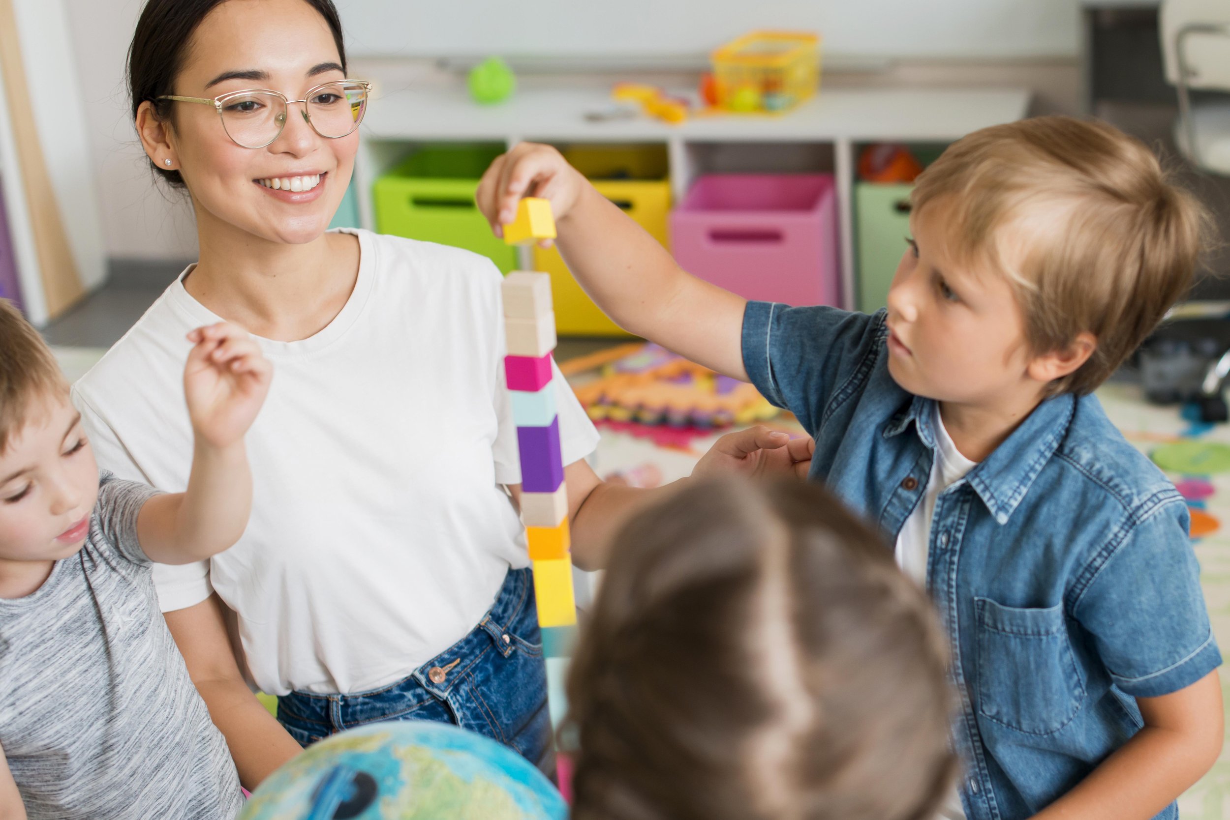 Young woman playing with colored blocks with a group of young children in a child care setting.