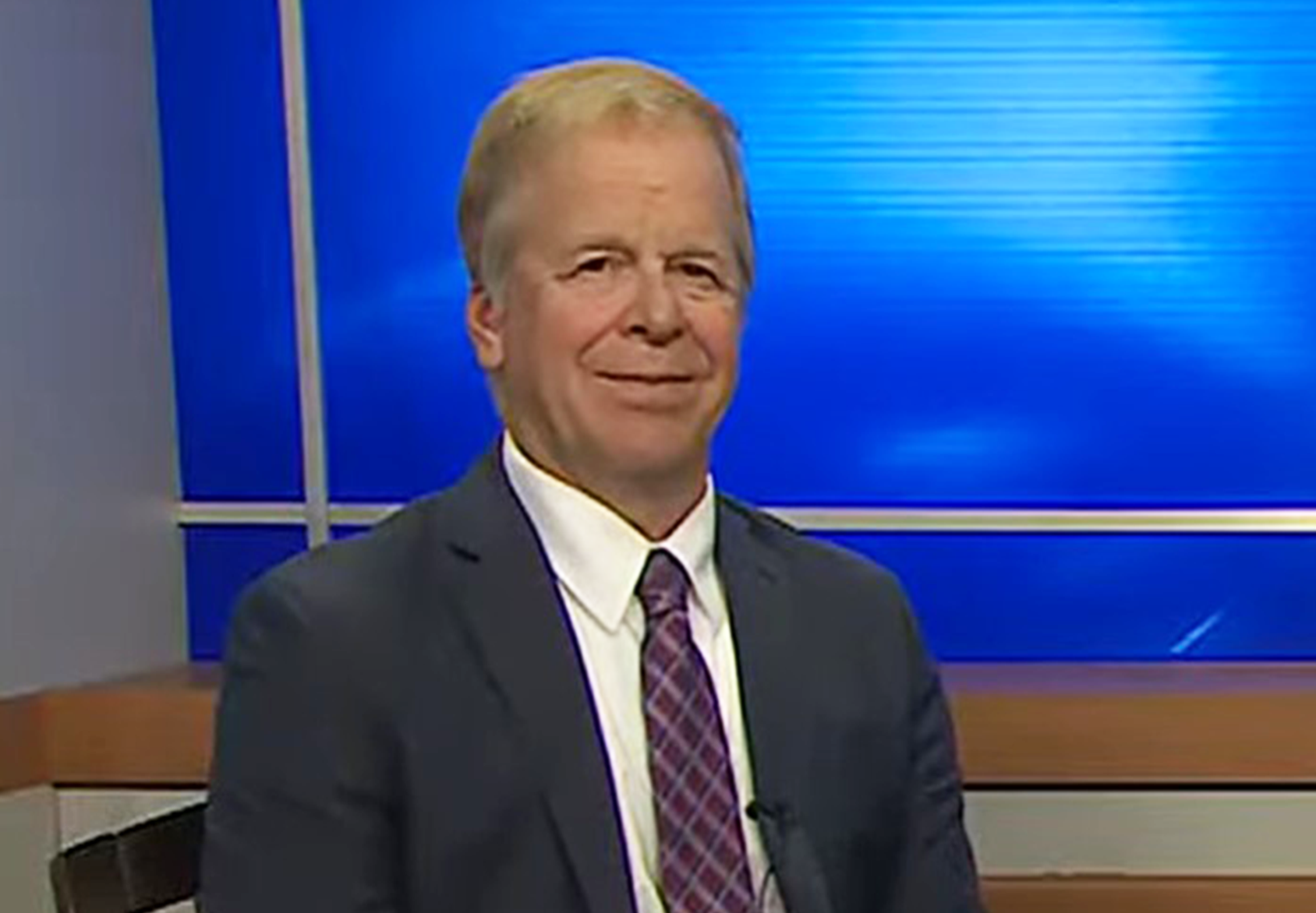 Image of a smiling man in a gray suit against a blue background.
