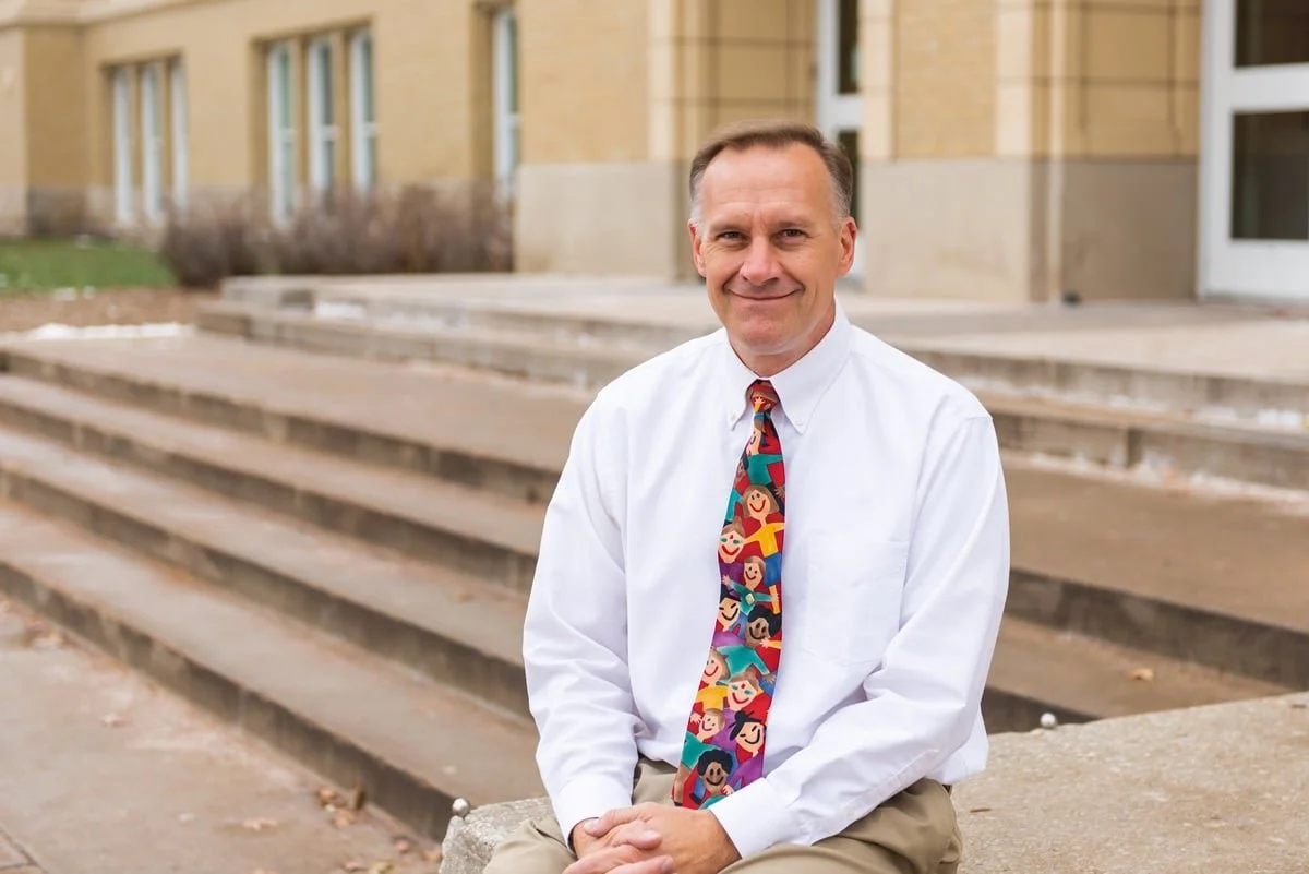 Smiling man in a white shirt with a colorful tie sitting on stone steps.