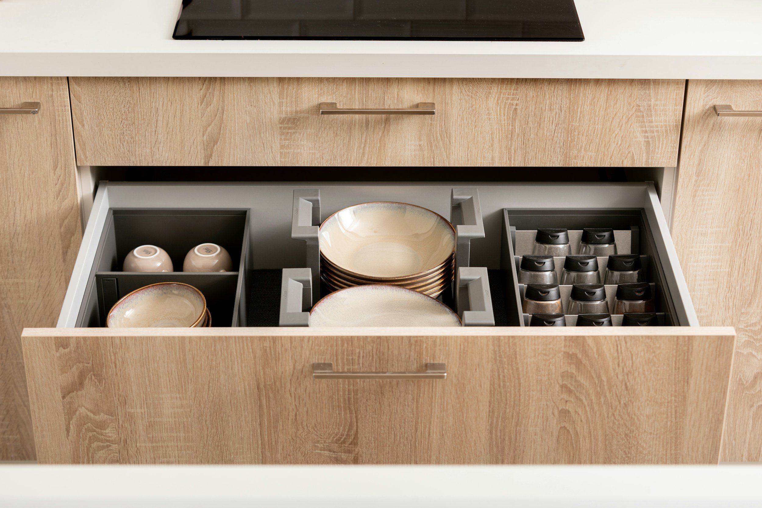 Open kitchen drawer with arranged dishes, bowls, and spice jars. High-end cabinetry with high-end products to keep the dishes in an organized manner.