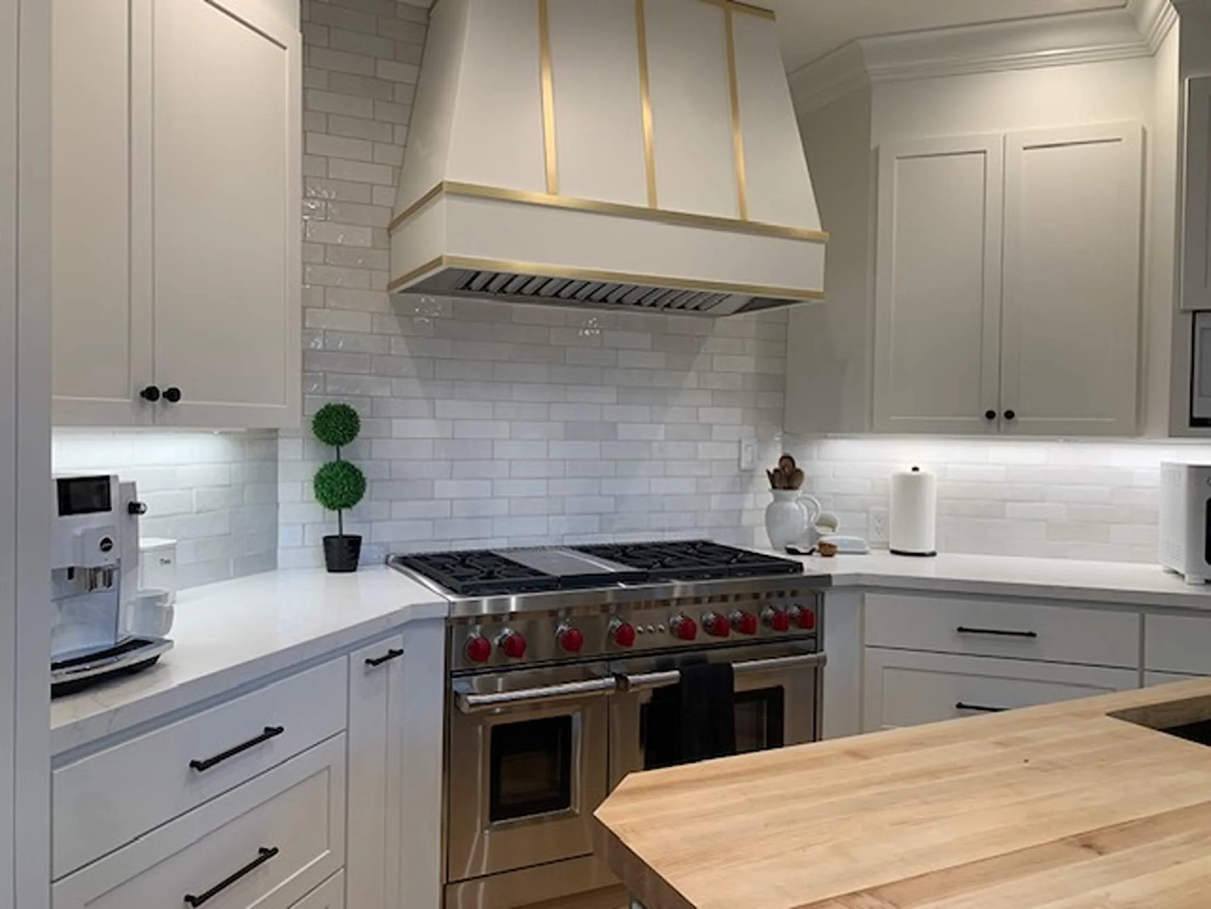 Modern kitchen with white cabinets, stainless steel stove, white backsplash, coffee maker, paper towel roll, decorative topiary, and wooden countertop island.
