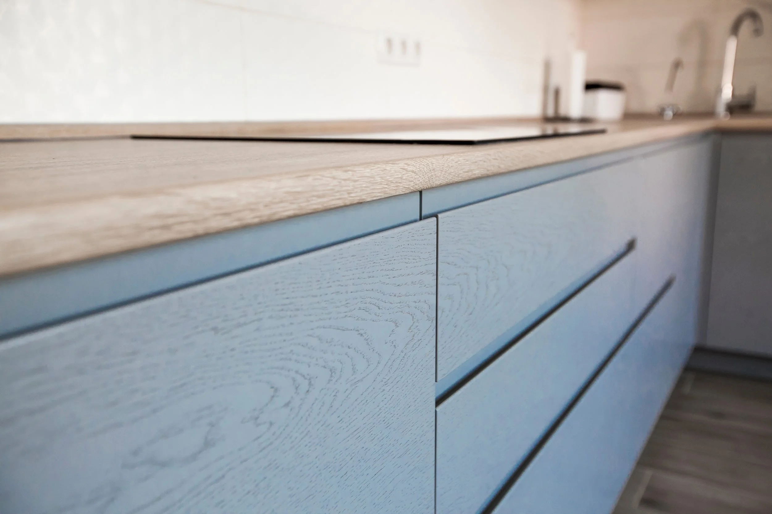 Close-up of a kitchen cabinet with a light blue painted wood finish and a light wood countertop.