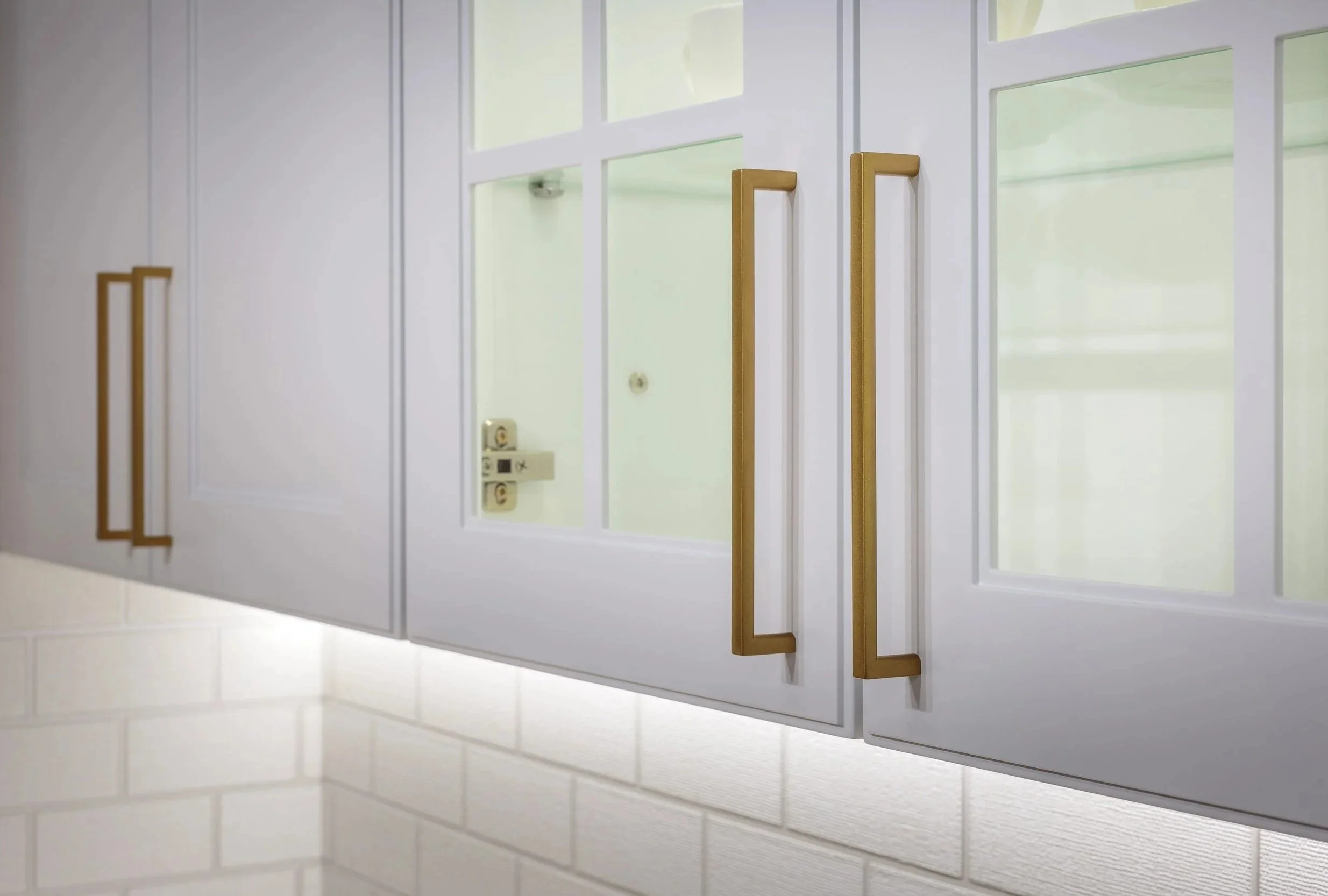 Close-up of white kitchen cabinets with gold handles, and a glass door showing a door lock outside.