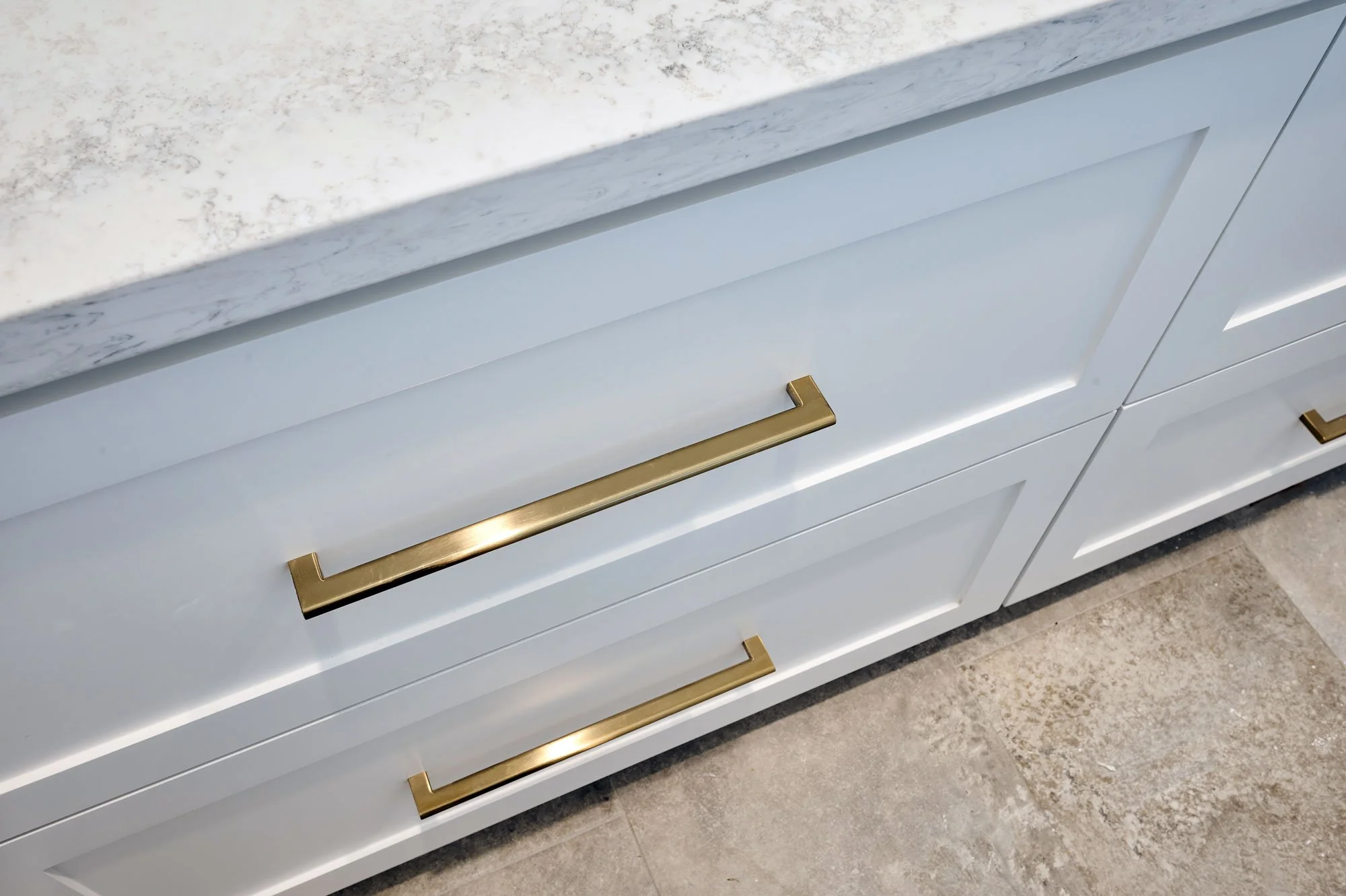 Close-up of a modern white cabinet with gold handles and a white marble countertop with grey veining.