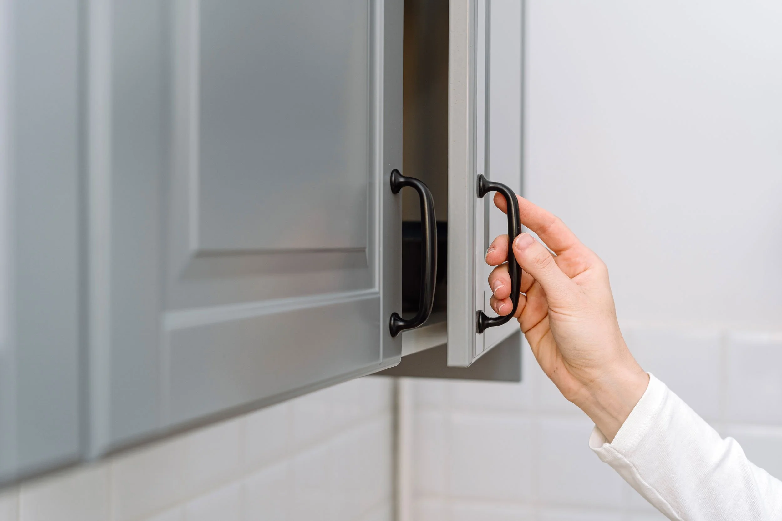 A person opening a gray cabinet with black handles in a kitchen or bathroom.