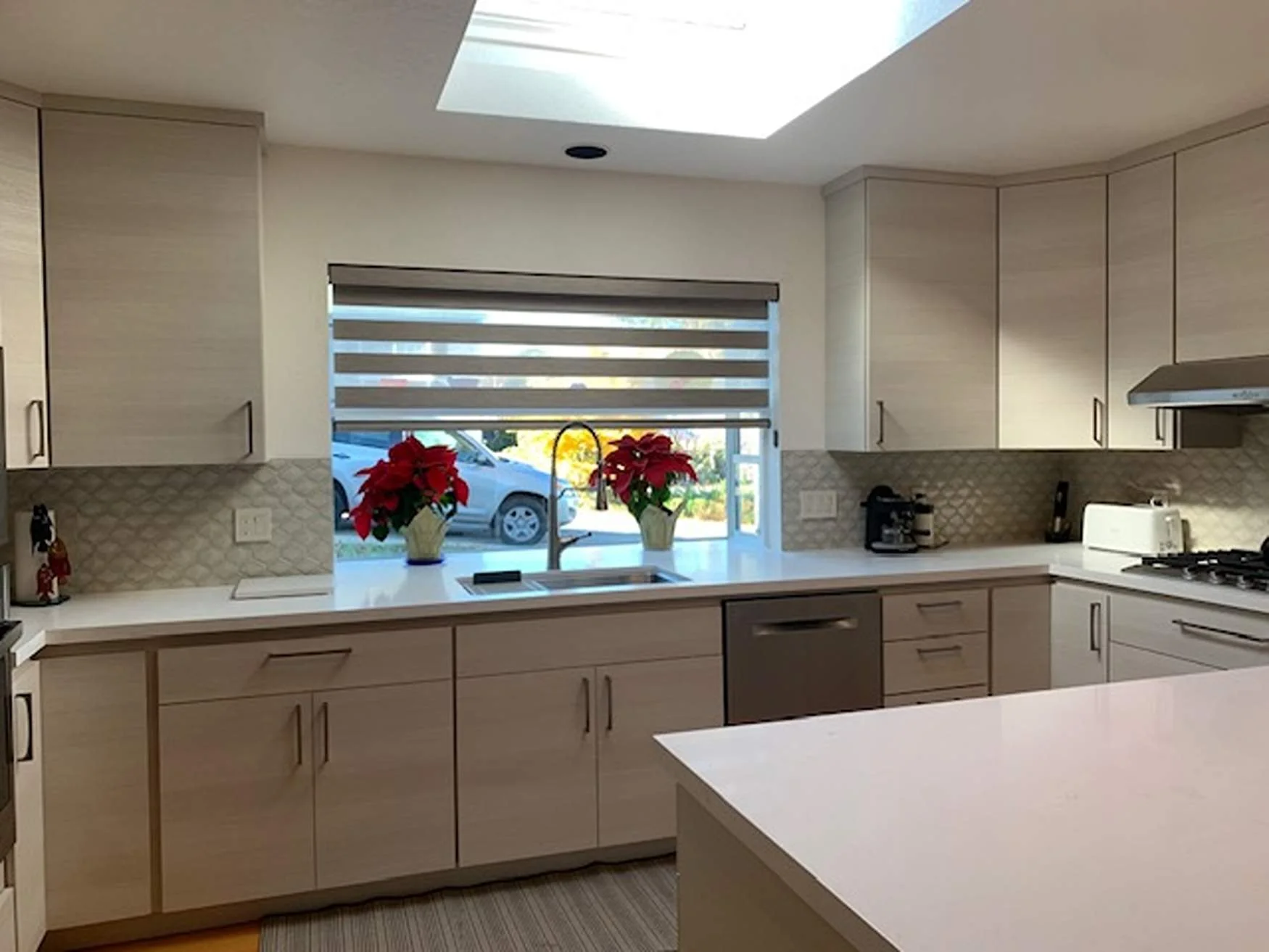 Modern kitchen with white cabinets, a window with two poinsettia plants, and various small appliances.