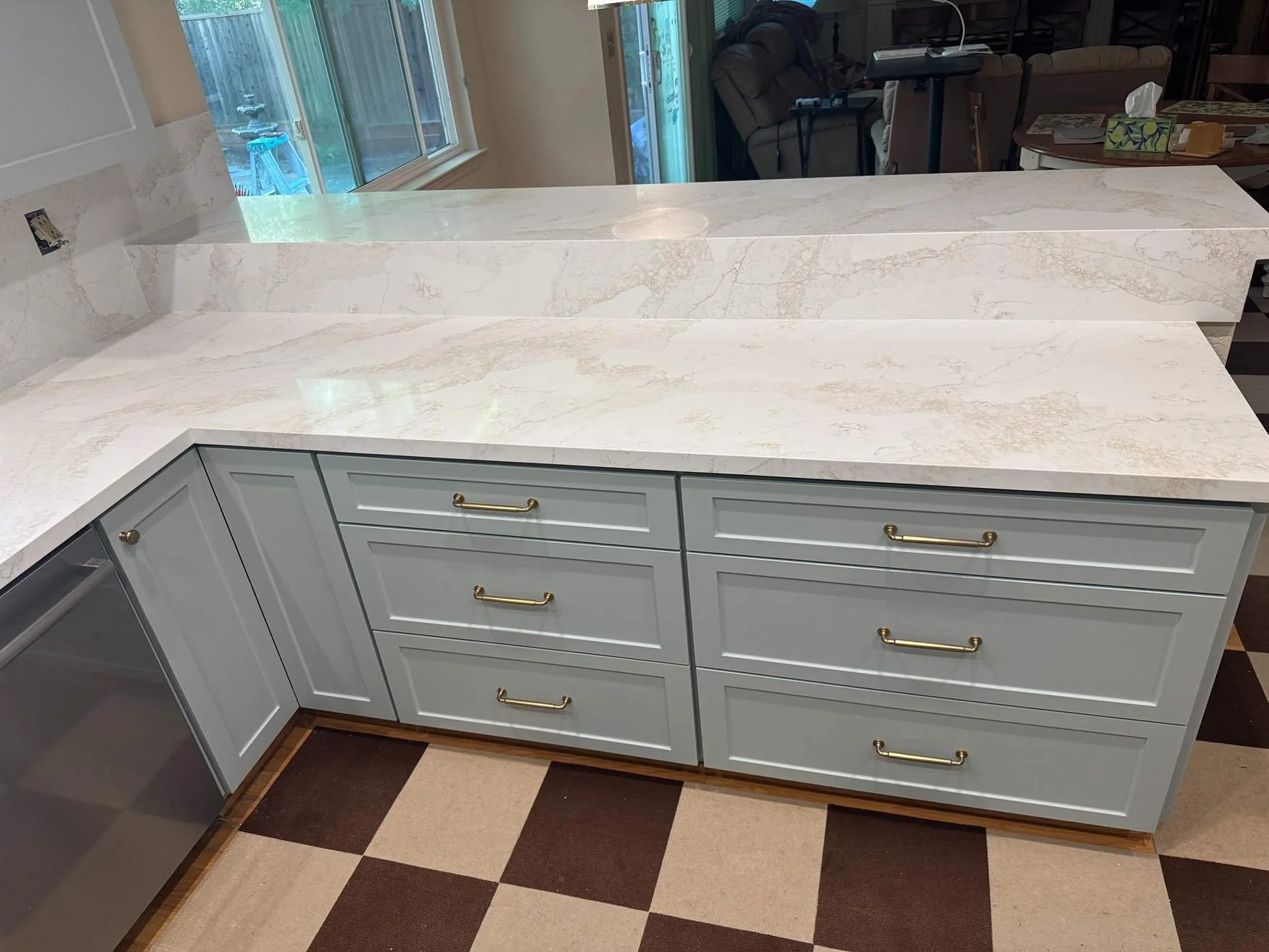 Kitchen island with light blue cabinetry and gold handles, topped with white marble countertop with beige veining, in a kitchen with checkered tile floor.