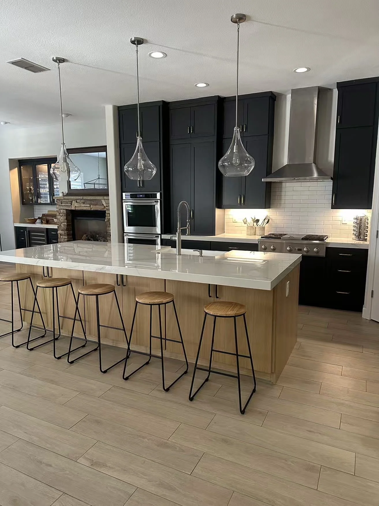 Modern kitchen with black cabinets, white countertop island with wooden stools, and pendant lighting.