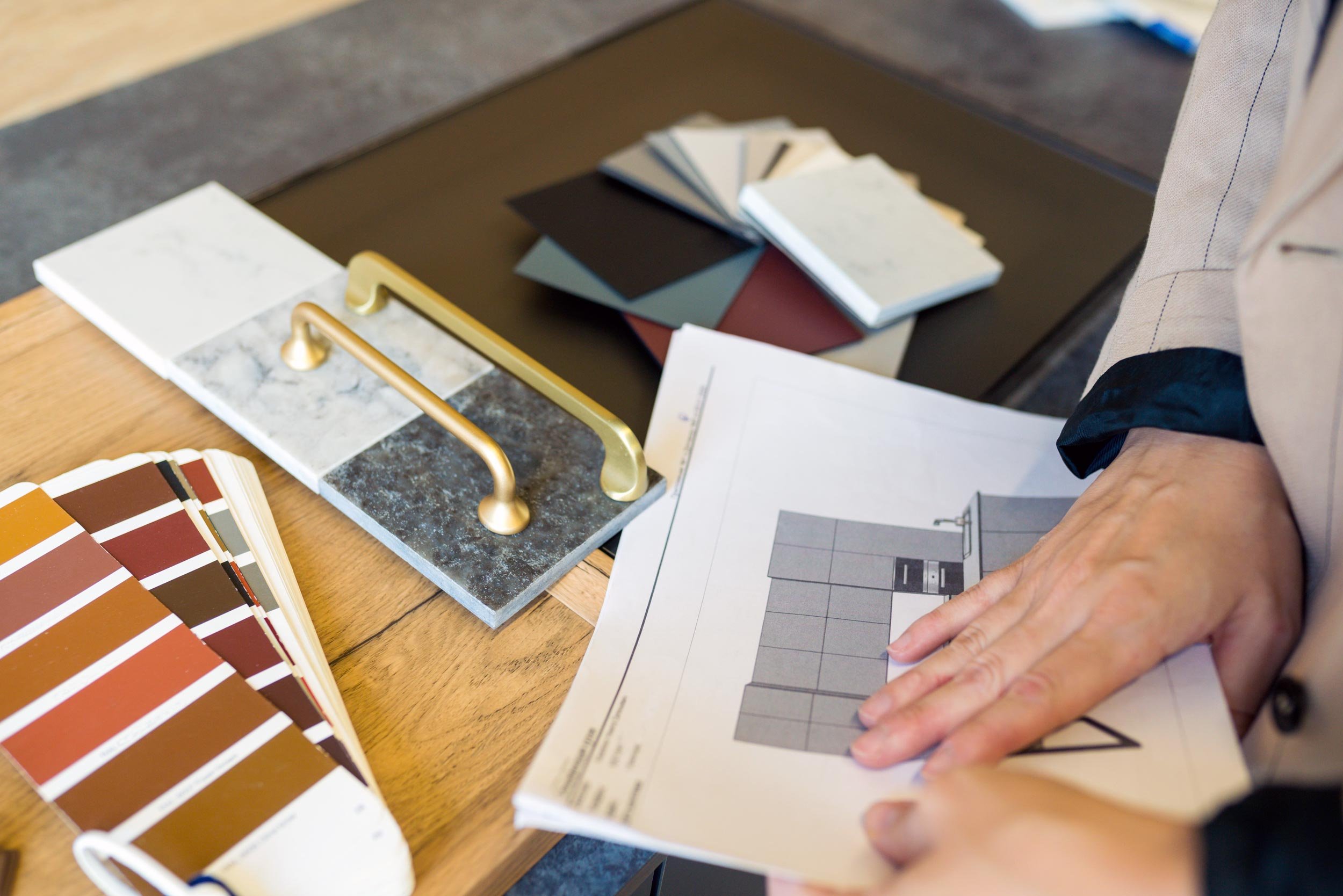 Person examining color and material samples, including paint swatches and tile options, while reviewing a building or interior design plan.