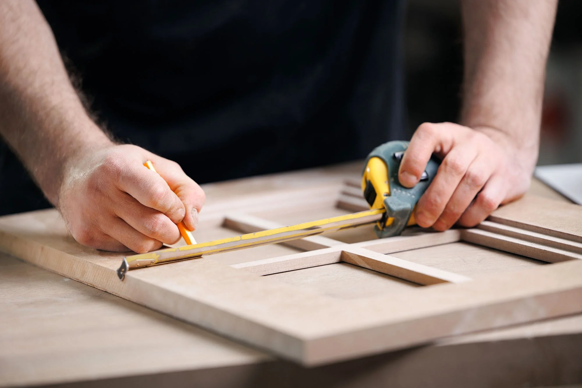 Person measuring and drawing markings on a wooden kitchen door with a tape measure and pencil.