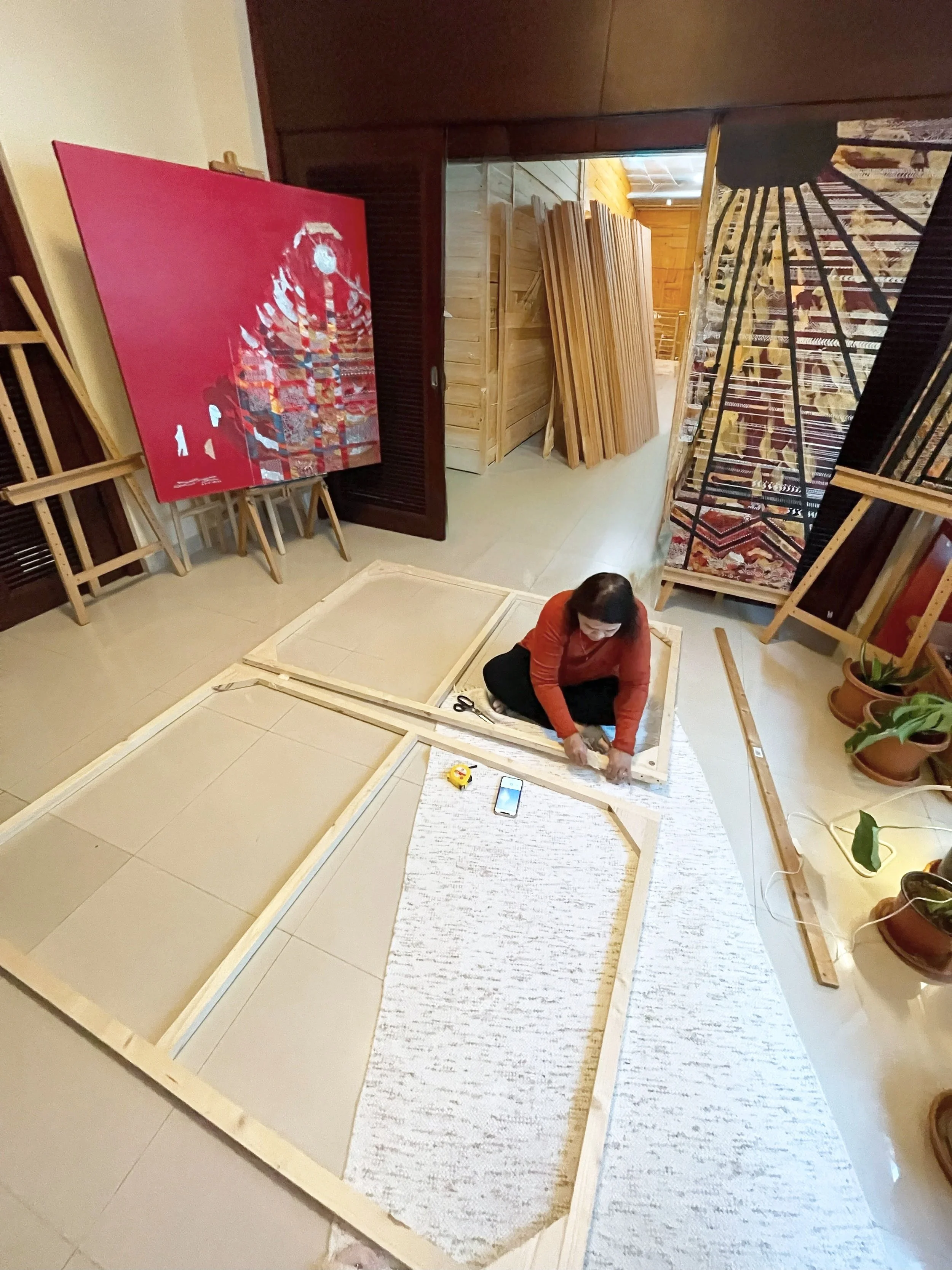 Woman assembling wooden frames on a floor with various artworks and paintings in the background.