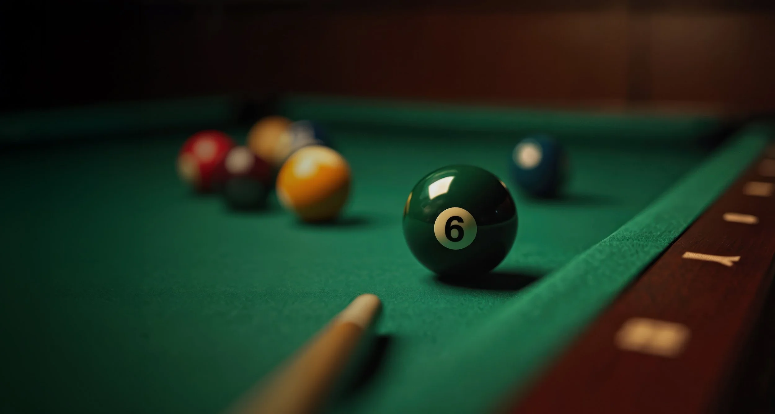 Green new pool table with billiard balls, including the 6 ball in focus, and a cue stick resting on the table edge.