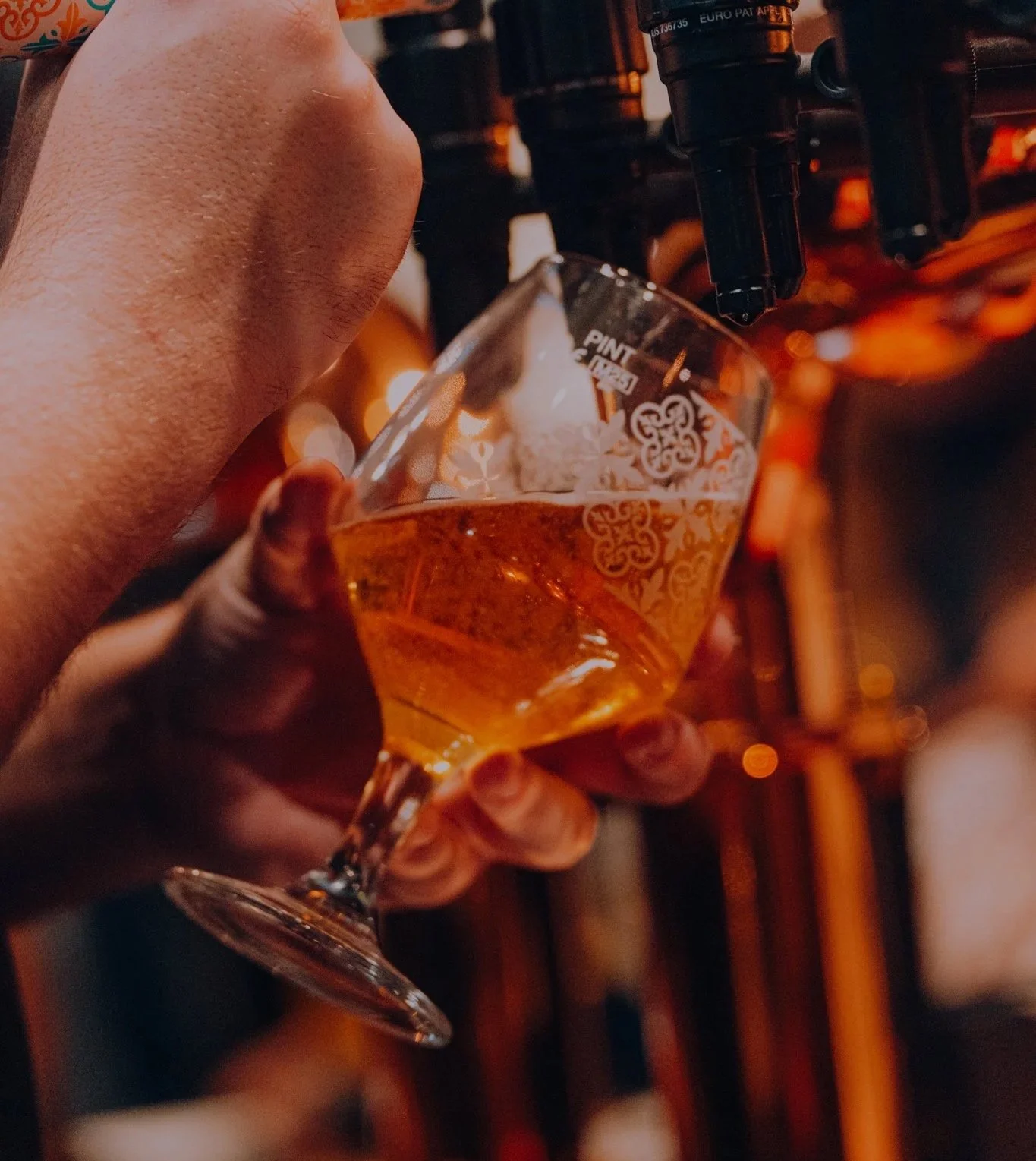 Person holding a tulip-shaped glass of amber-colored beer under a tap at a bar. Pub in Newcastle, Killingworth.