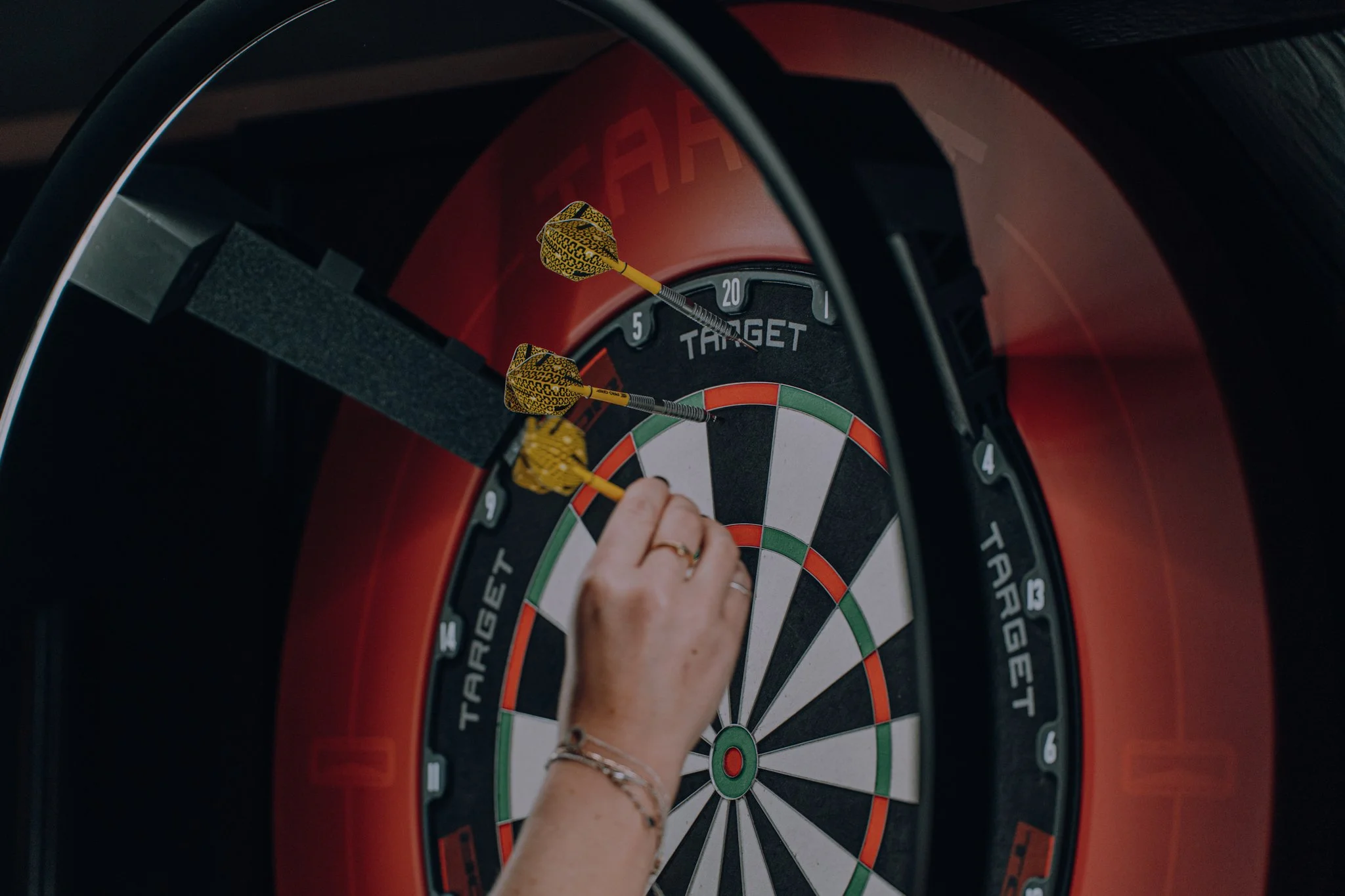 A person’s hand adjusting darts on a dartboard, with a black and red target.