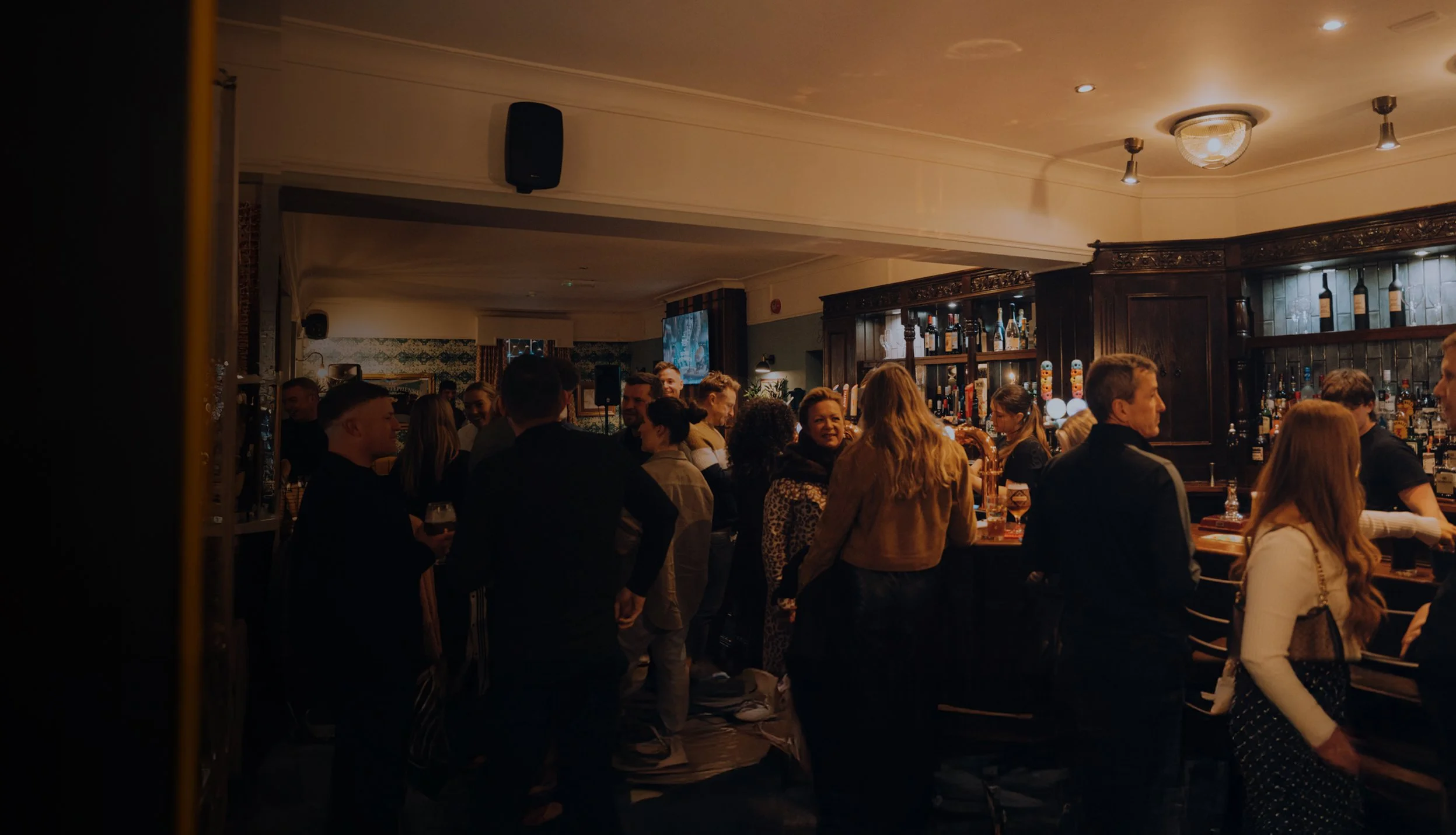 People socializing in a cozy pub in Killingworth, Newcastle with dark wood decor and a well-stocked bar counter. The George Stephenson.