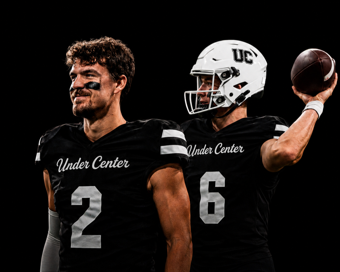 Two football players in black uniforms with white accents and the text "Under Center". One player with jersey number 2 and the other with 6. The player with jersey 6 is wearing a helmet and holding a football.