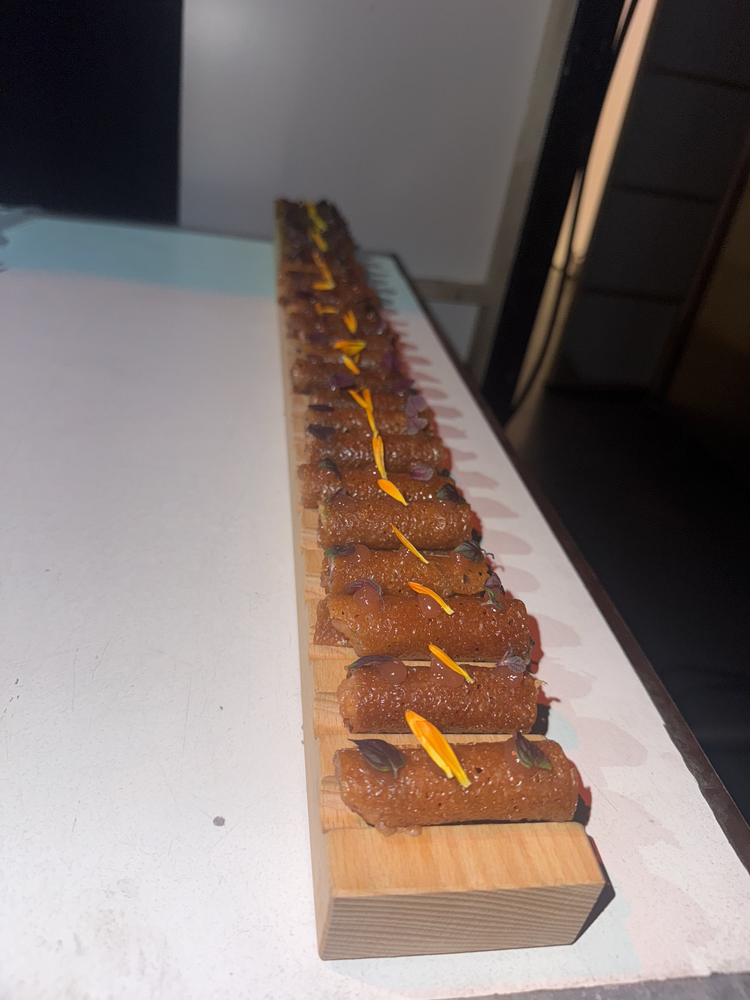 Row of small pastries with yellow garnish and herbs on wooden board.