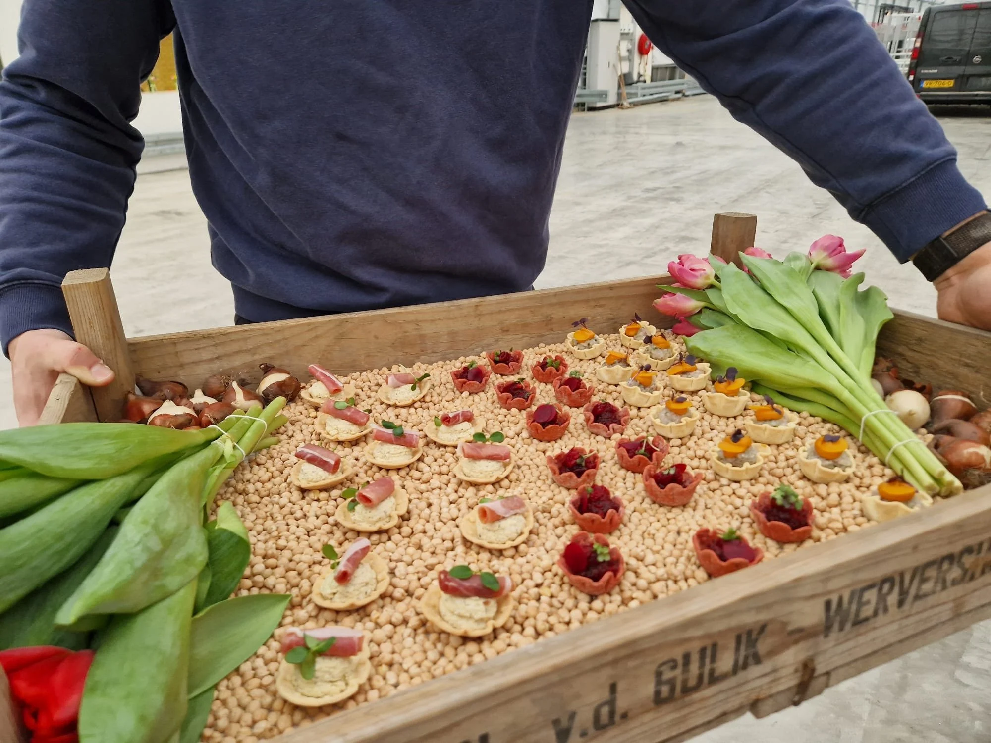 A person holding a wooden tray filled with small floral arrangements and tulips.