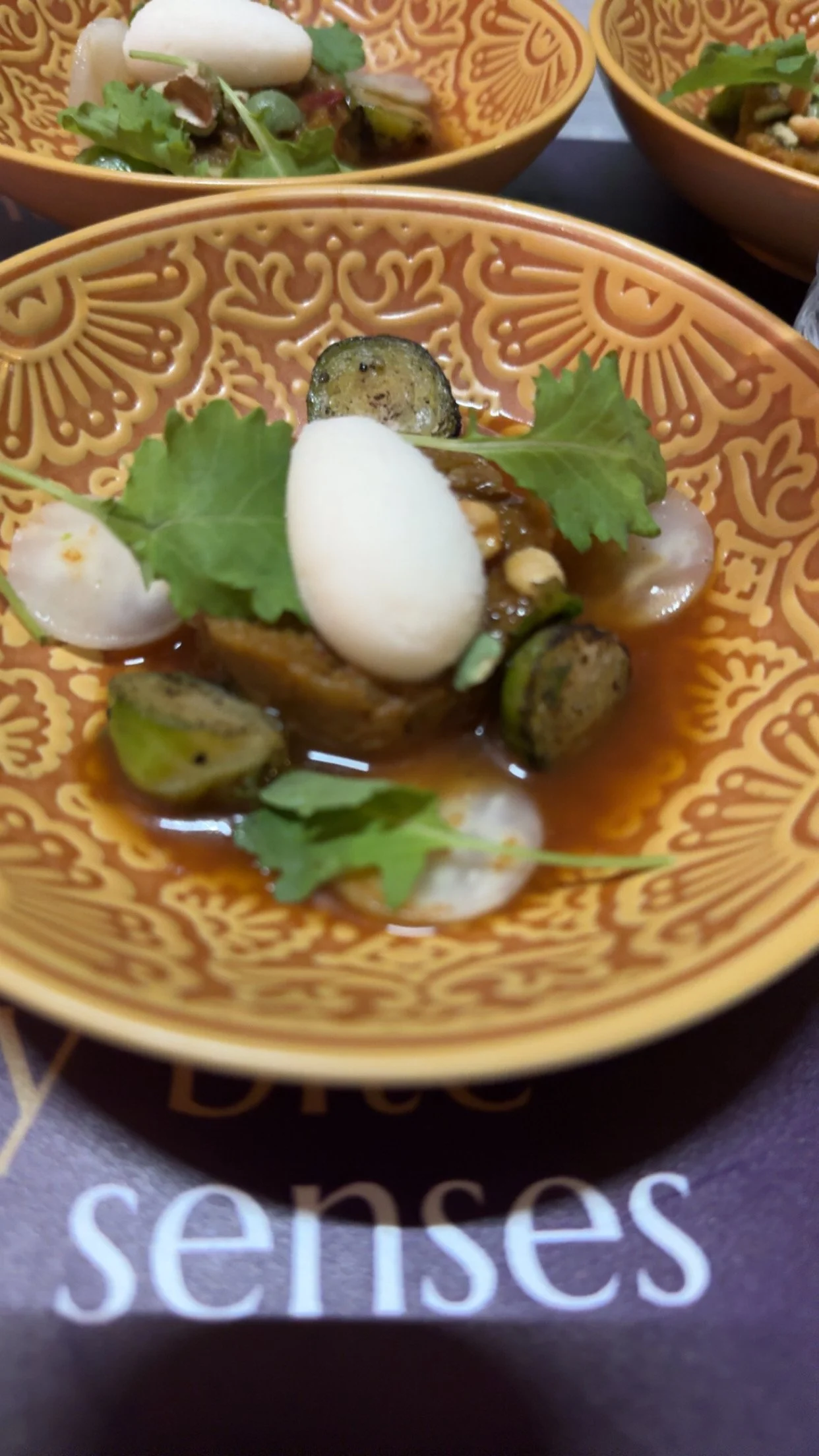 A bowl of Mexican street corn with grilled zucchini, topped with a white sauce or crema, garnished with cilantro and radish slices.