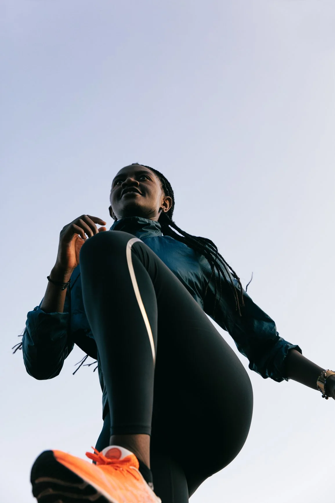 Low-angle view of a woman in athletic clothing, standing outdoors against a clear sky.