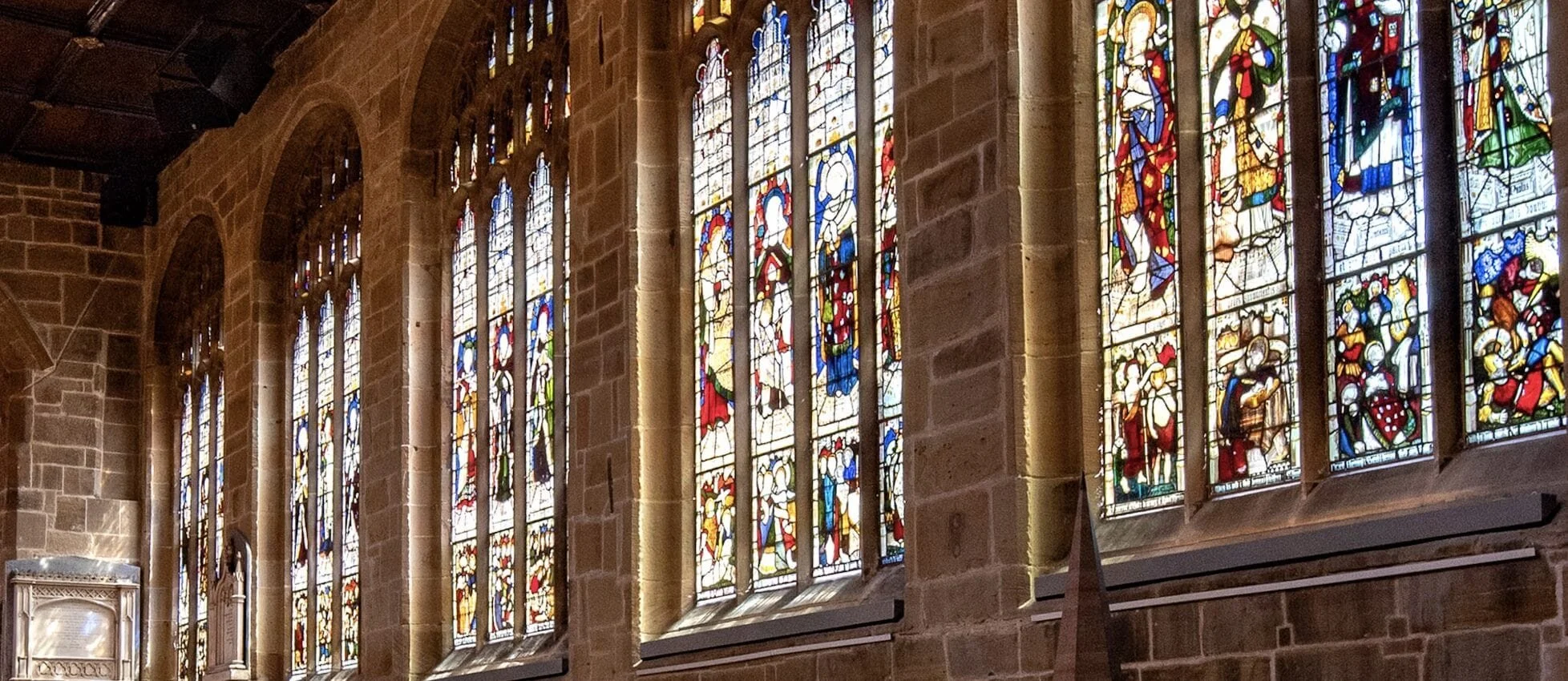 Colorful stained glass windows depicting religious figures and scenes inside a church with stone walls.