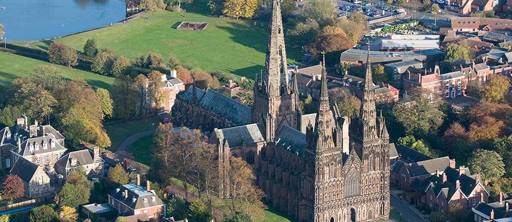 Aerial view of a historic Gothic cathedral surrounded by residential houses and green parks, with colorful trees and streets in the background.