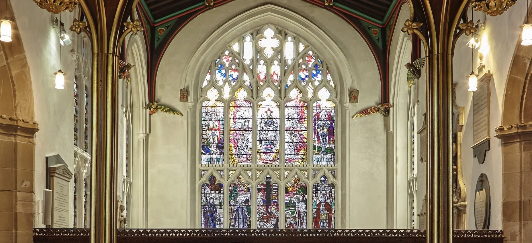 Inside a church with colorful stained glass windows depicting religious scenes, gothic arches, and decorative gold accents.