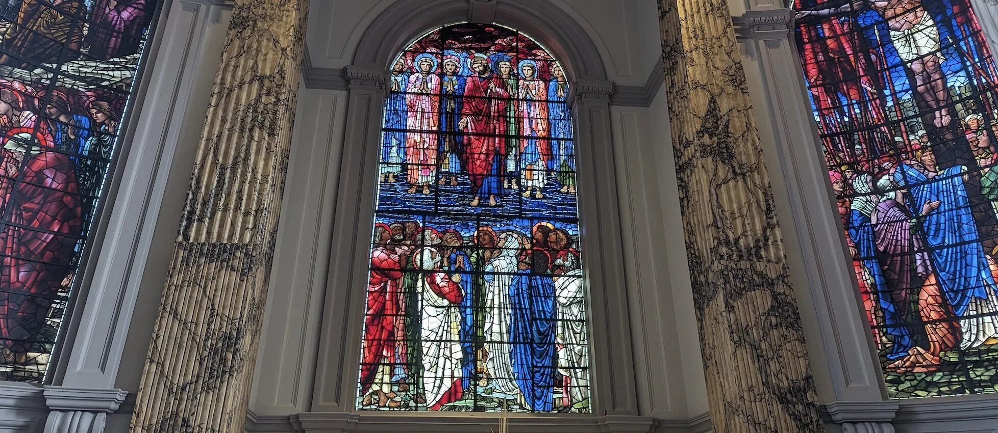 Colorful stained glass window depicting a religious scene with a central figure in red robes and four other figures below, surrounded by ornate architectural details.