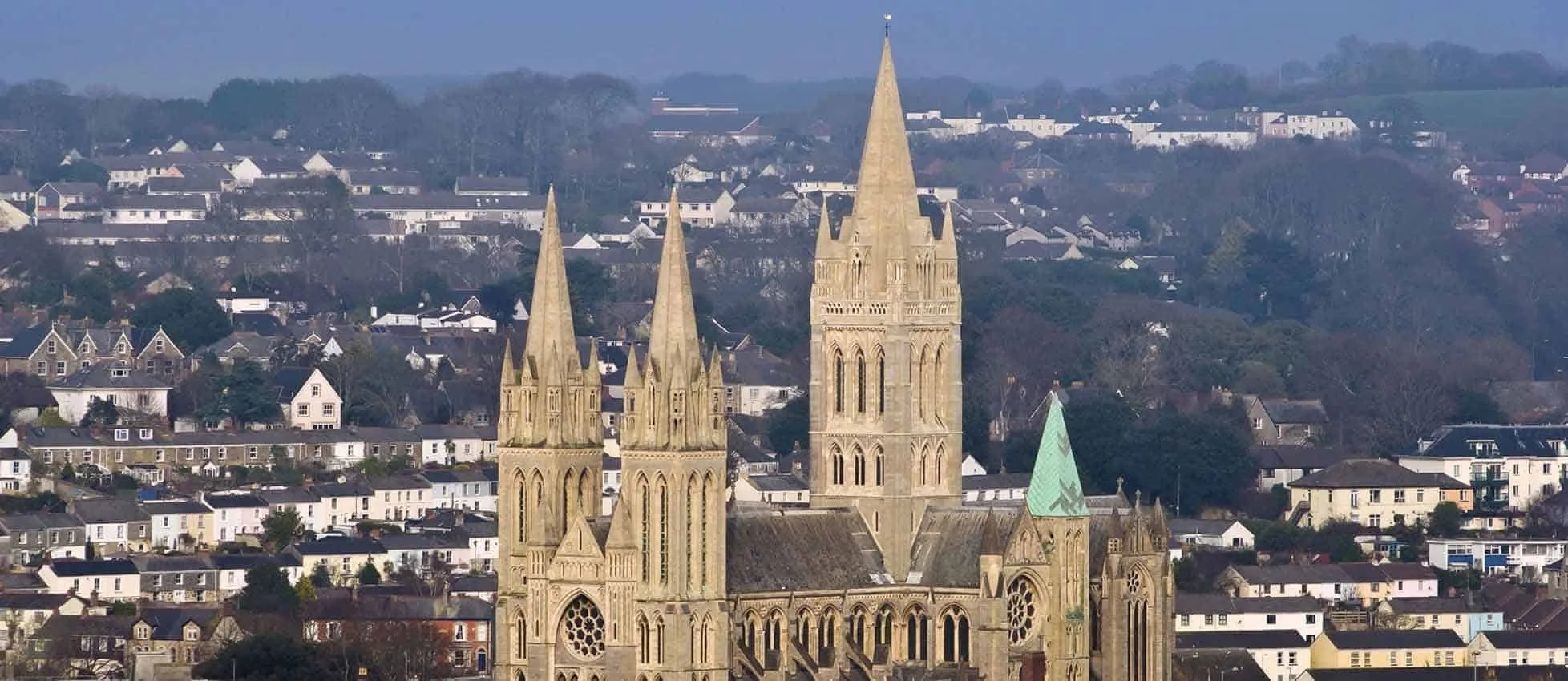 A large Gothic-style church with multiple tall spires in a cityscape, surrounded by residential buildings and green hills in the background.
