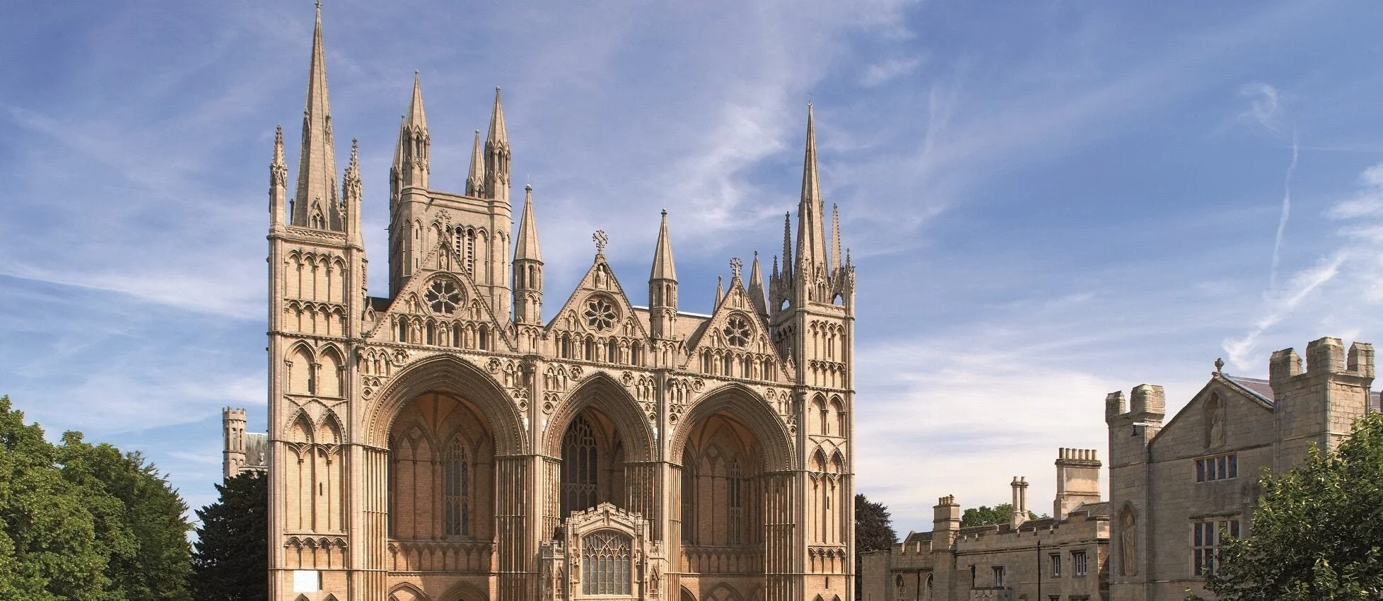 Front view of a Gothic cathedral with tall spires, ornate architecture, and large stained glass windows, set against a blue sky with some clouds.