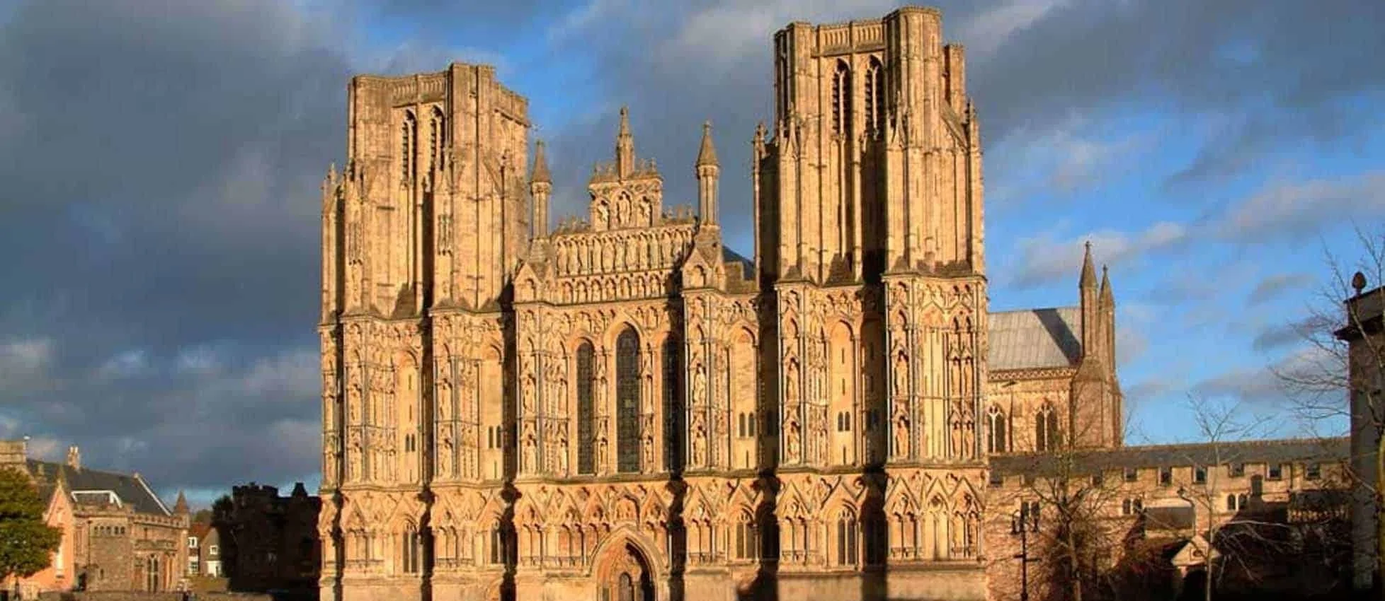 A large Gothic-style cathedral with intricate stonework and tall towers, illuminated by sunlight against a partly cloudy sky.