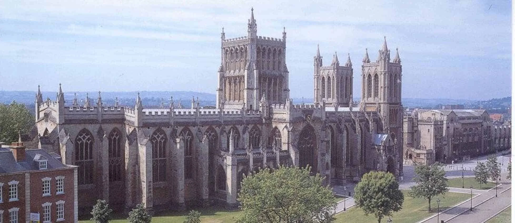 A historic Gothic-style cathedral with tall spires, large stained glass windows, and detailed stone architecture, situated in an urban area with a park and trees in the foreground.