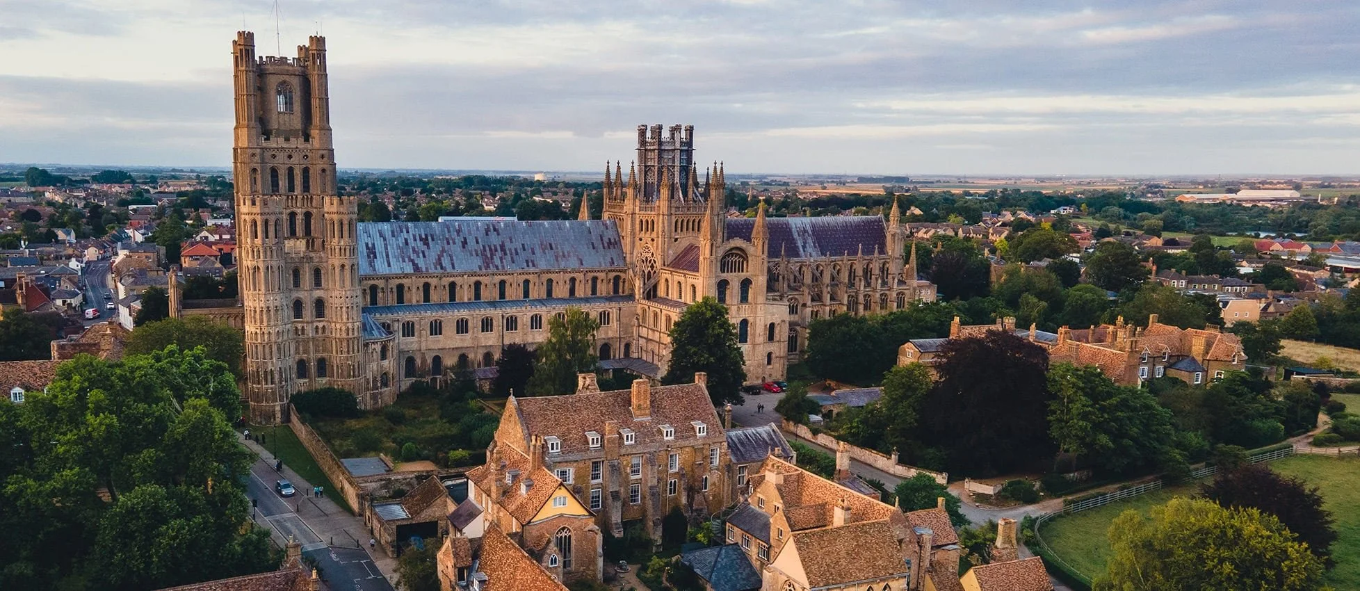 Aerial view of a historic Gothic cathedral with tall towers, surrounded by a small town with residential houses and green trees.