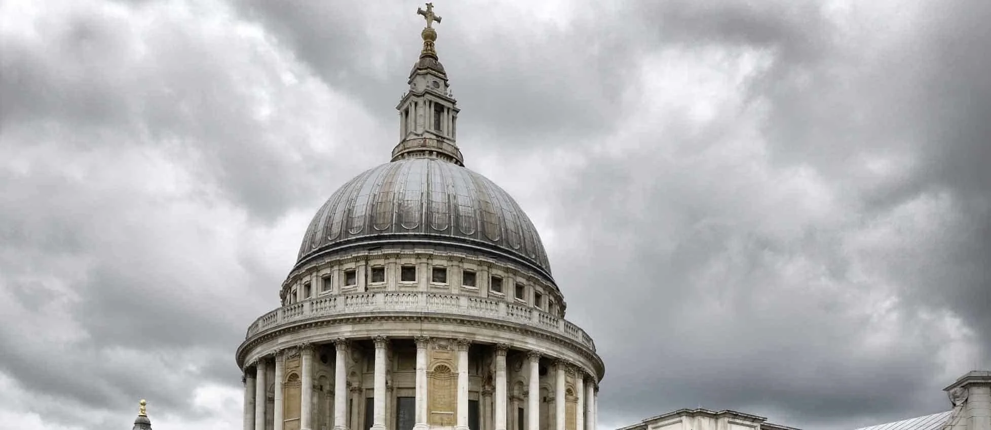 The dome of St. Paul's Cathedral with a statue at the top, set against a cloudy sky.