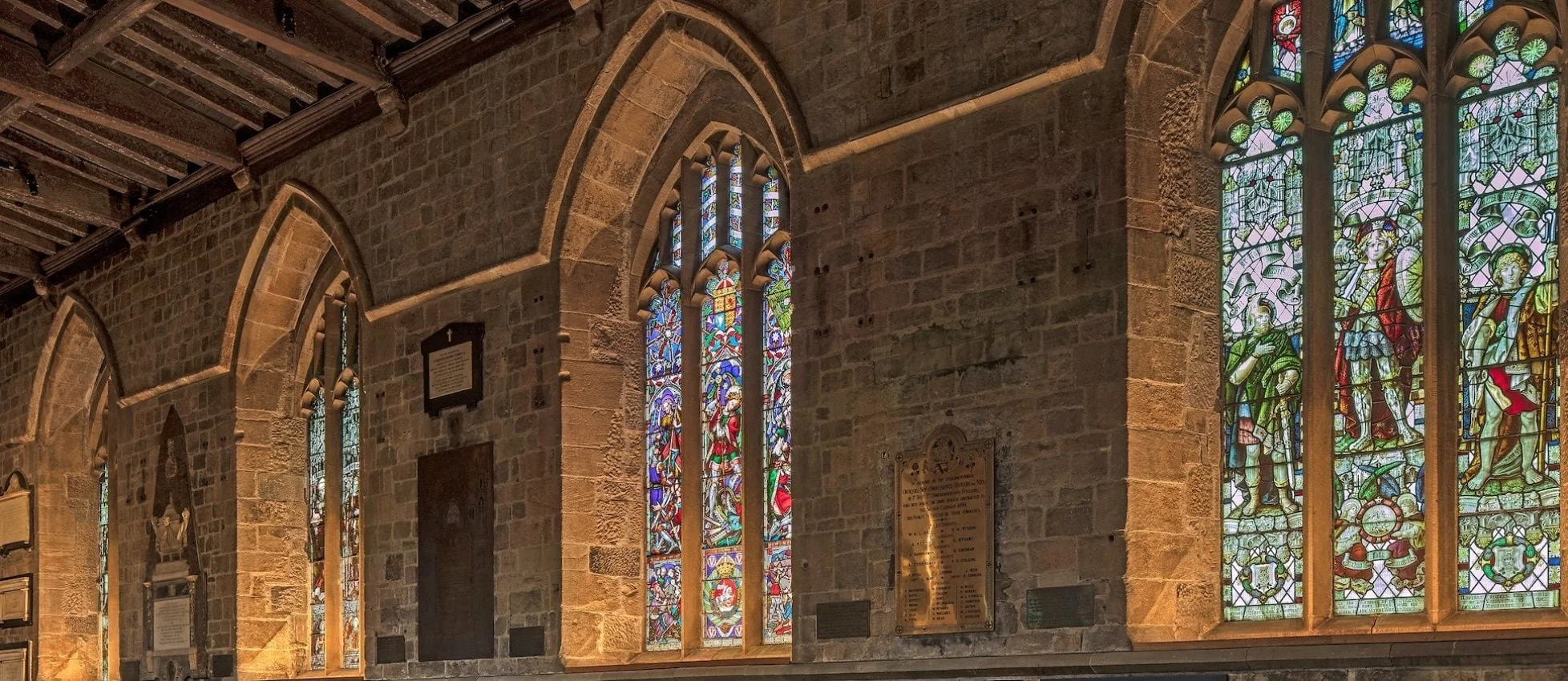 Stained glass windows in a stone church interior, with colorful biblical scenes and figures.