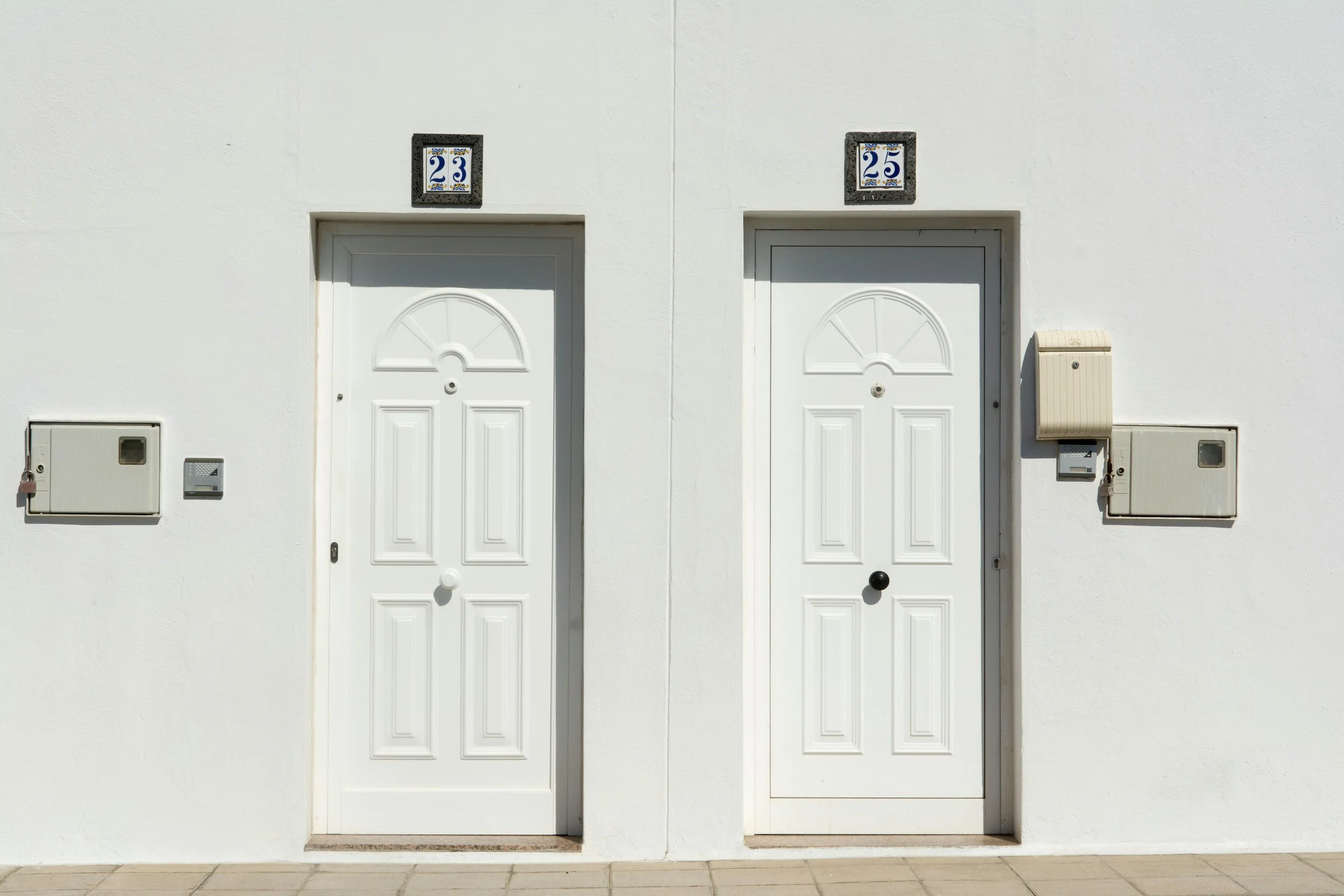 Side-by-side white doors with house numbers 23 and 25, and mailboxes mounted on the wall.