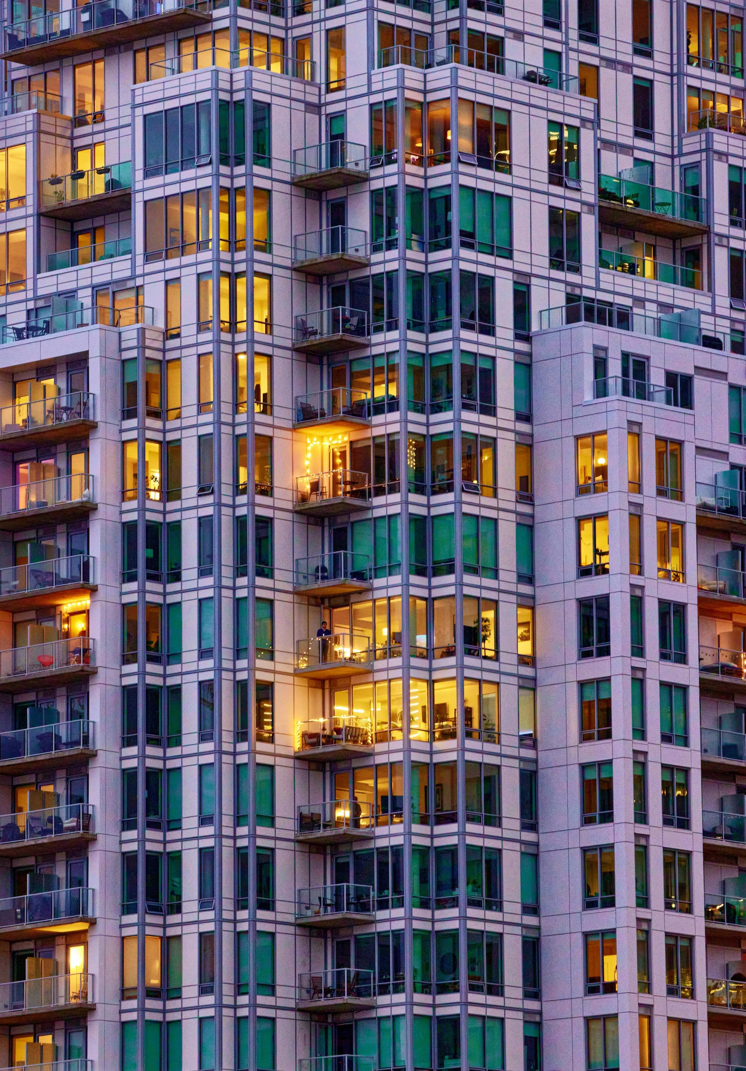 Close-up view of a high-rise apartment building with illuminated windows and balconies, showing a mixture of interior lights and decorated outdoor areas.